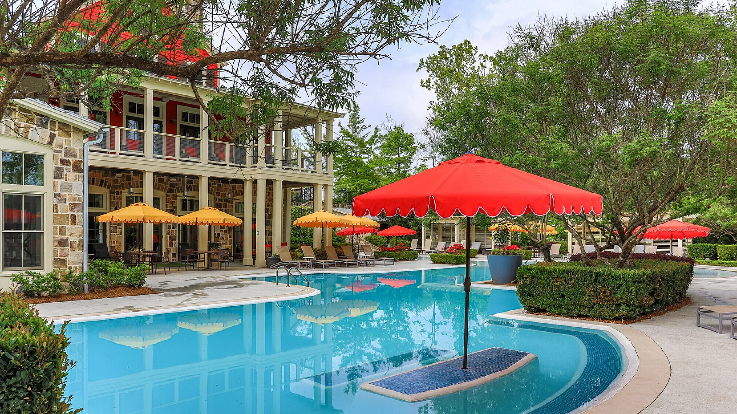 Inviting outdoor pool area with vibrant red and yellow umbrellas, surrounded by lush greenery and elegant architecture.