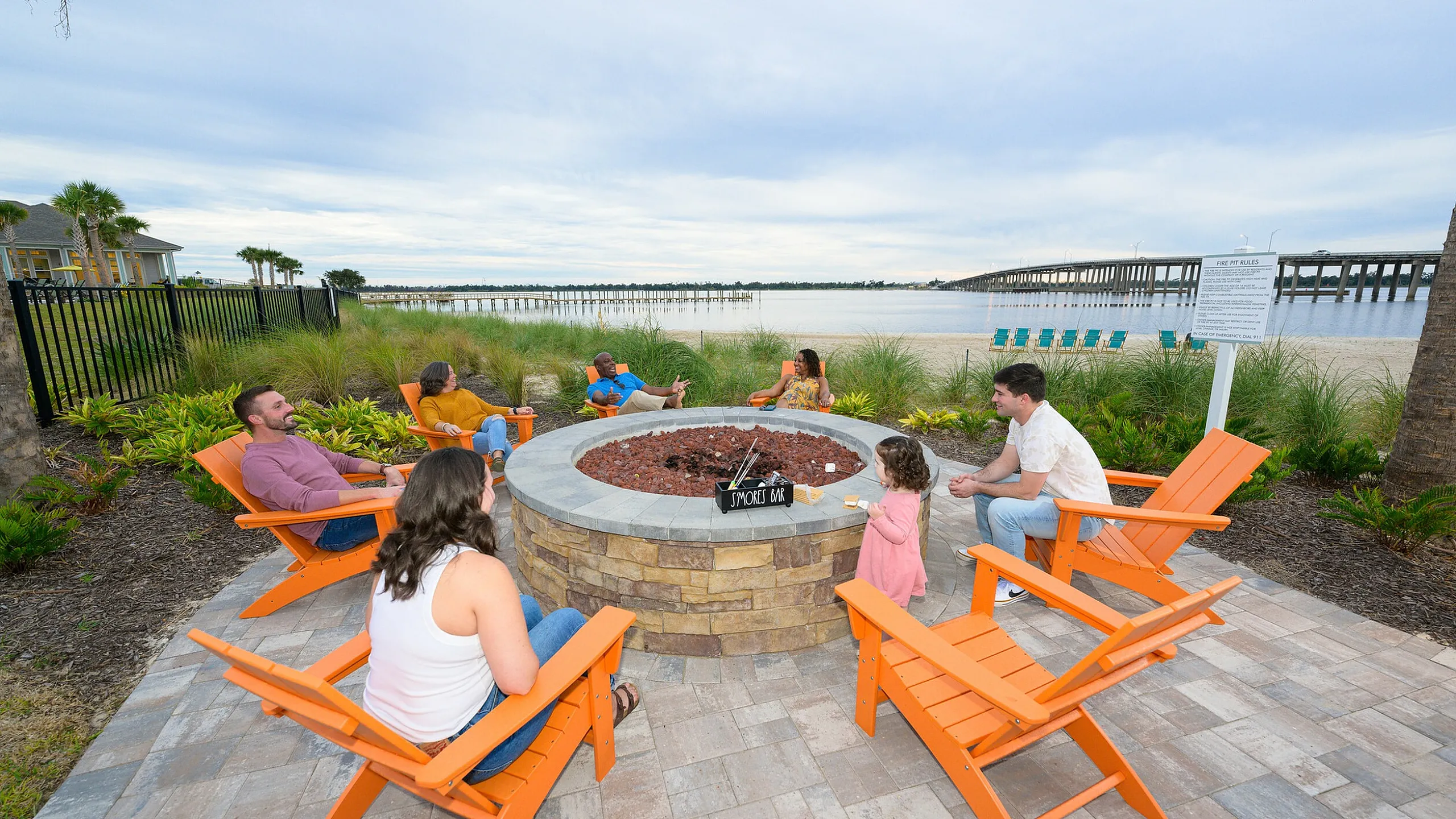 Vibrant outdoor fire pit area with orange Adirondack chairs by the water, offering a scenic riverside view perfect for gatherings.