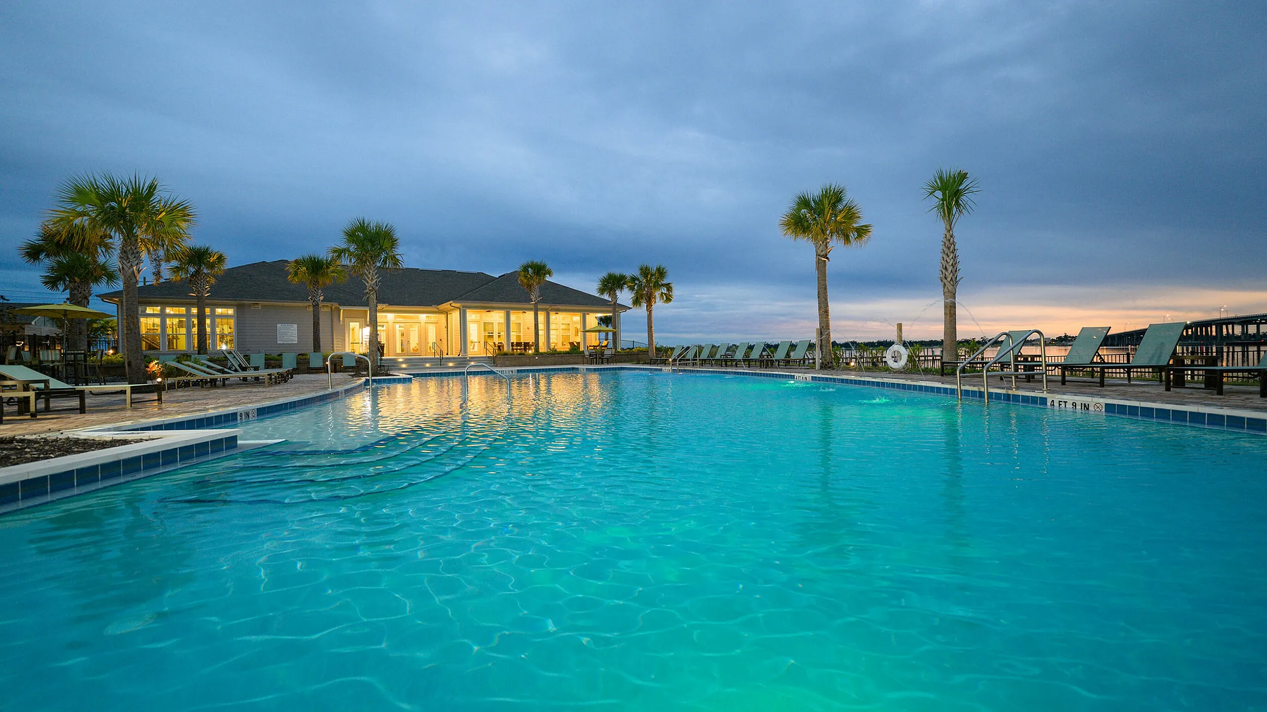 Luxurious poolside view with illuminated water, palm trees, and inviting lounge chairs, perfect for relaxation and leisure.