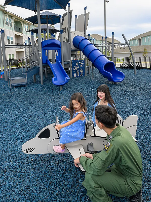Modern playground with vibrant blue slides and an airplane-themed seat, offering a fun and safe environment for children; attractive residential buildings in the background enhance the community feel.