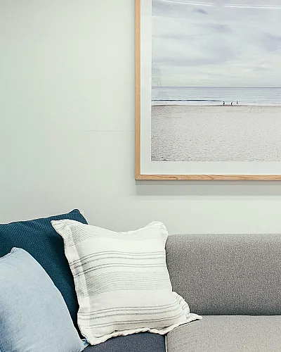 Inviting living room with a cozy gray and blue sofa adorned with soft pillows, complemented by a serene beach landscape artwork on the wall.