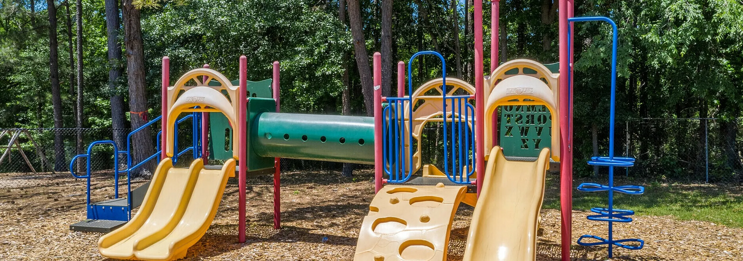 Bright and colorful playground surrounded by lush trees, featuring slides and climbing structures for family fun.