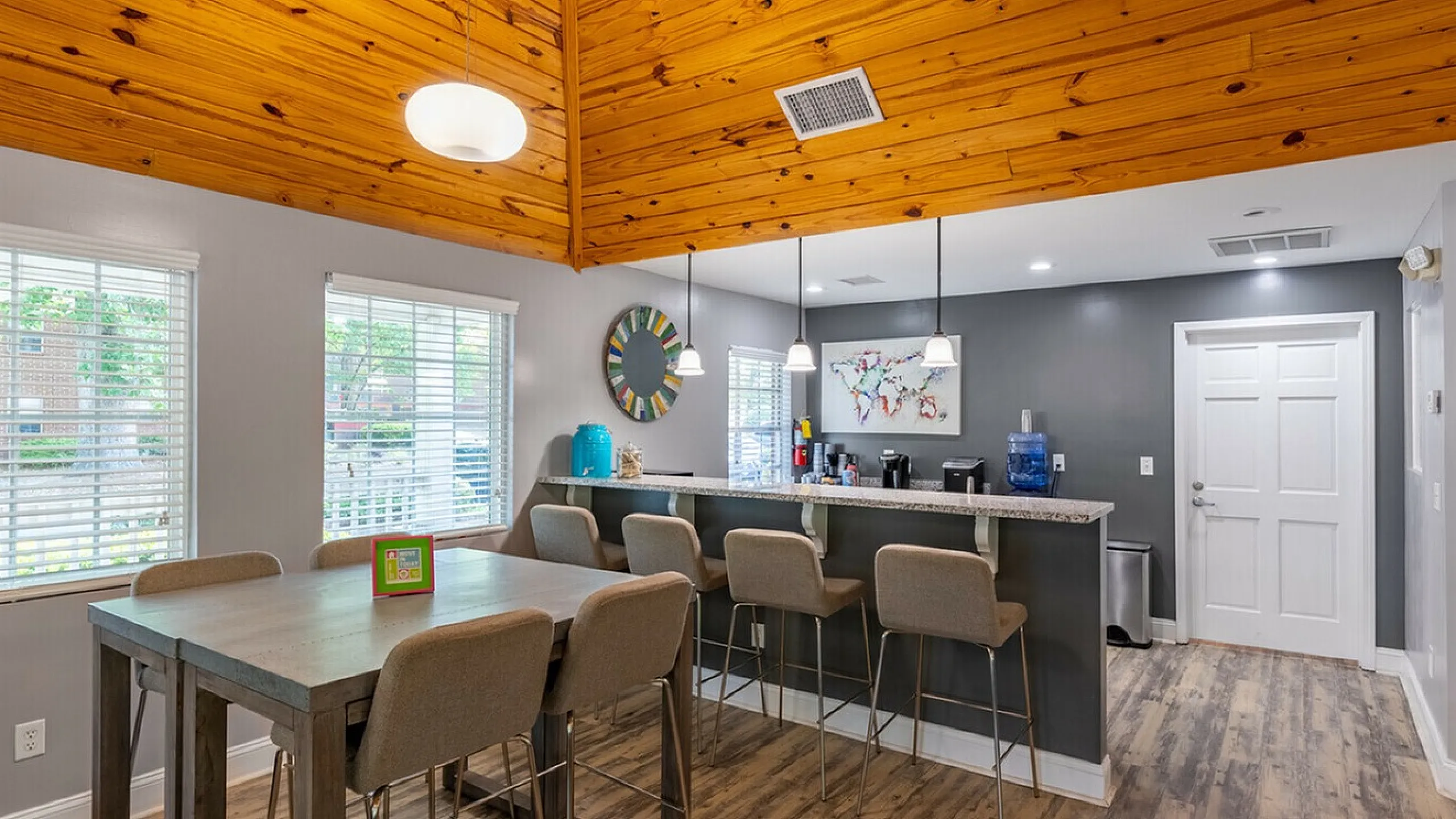 Inviting open-concept dining area with modern high chairs and a rustic wooden ceiling, illuminated by soft pendant lights.