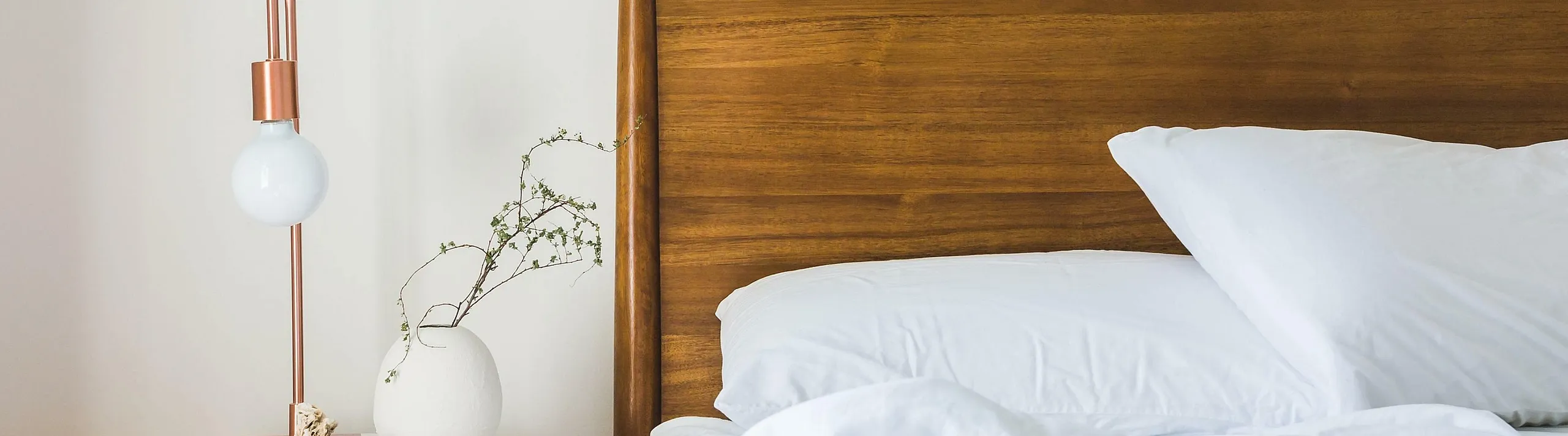 Elegant bedroom with a wooden headboard, crisp white bedding, and a stylish side table with a modern lamp and decorative vase.