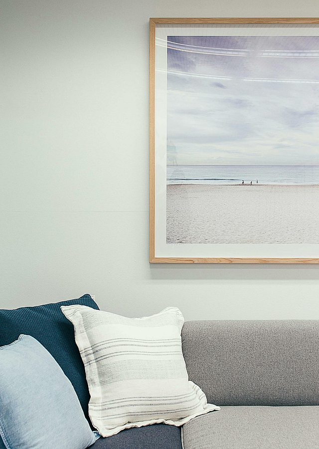 Cozy living room corner with stylish gray sofa, accent pillows, and serene beach artwork.