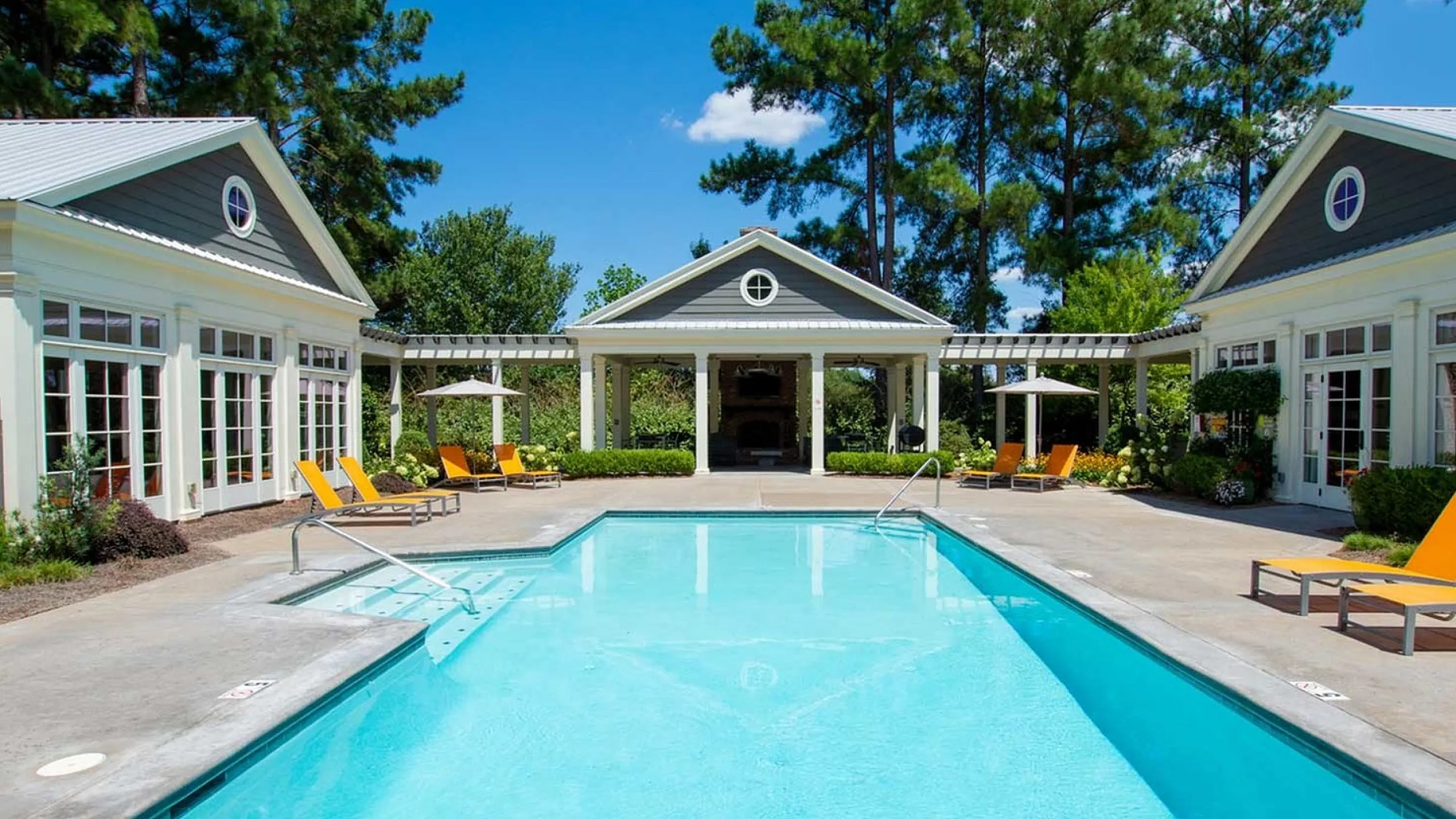 Luxurious outdoor pool surrounded by elegant buildings and lush greenery, offering serene relaxation under blue skies.