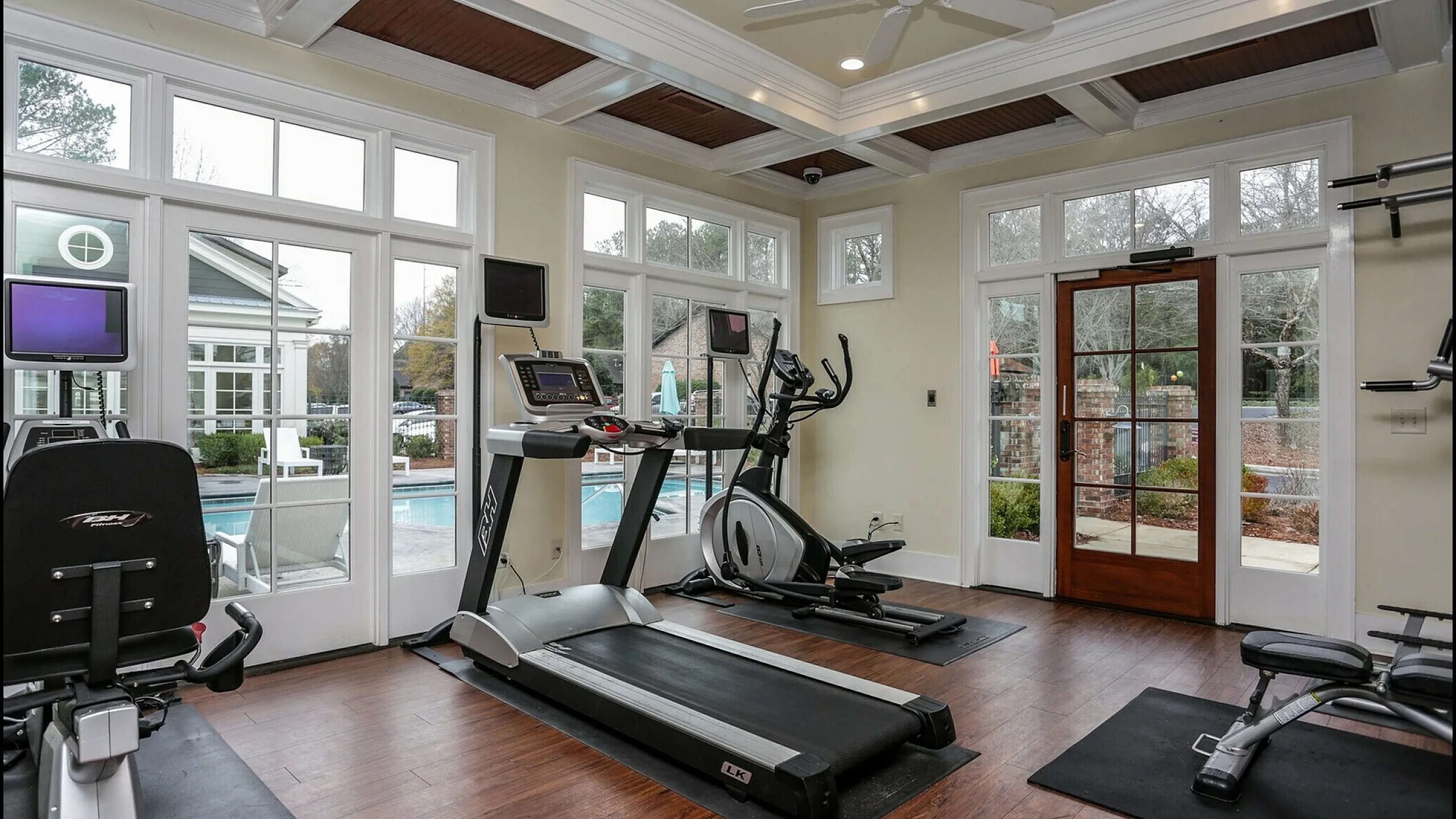 Bright and modern home gym with top-tier equipment, featuring large windows overlooking a serene pool area.