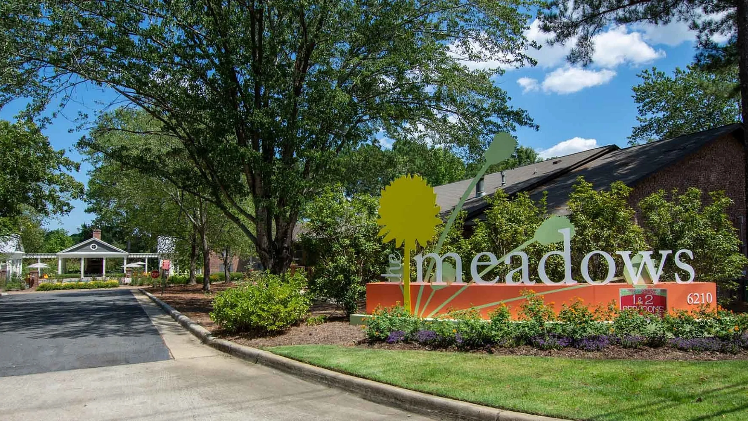 Charming entrance to 'The Meadows' apartment community, surrounded by lush greenery and vibrant flower beds.