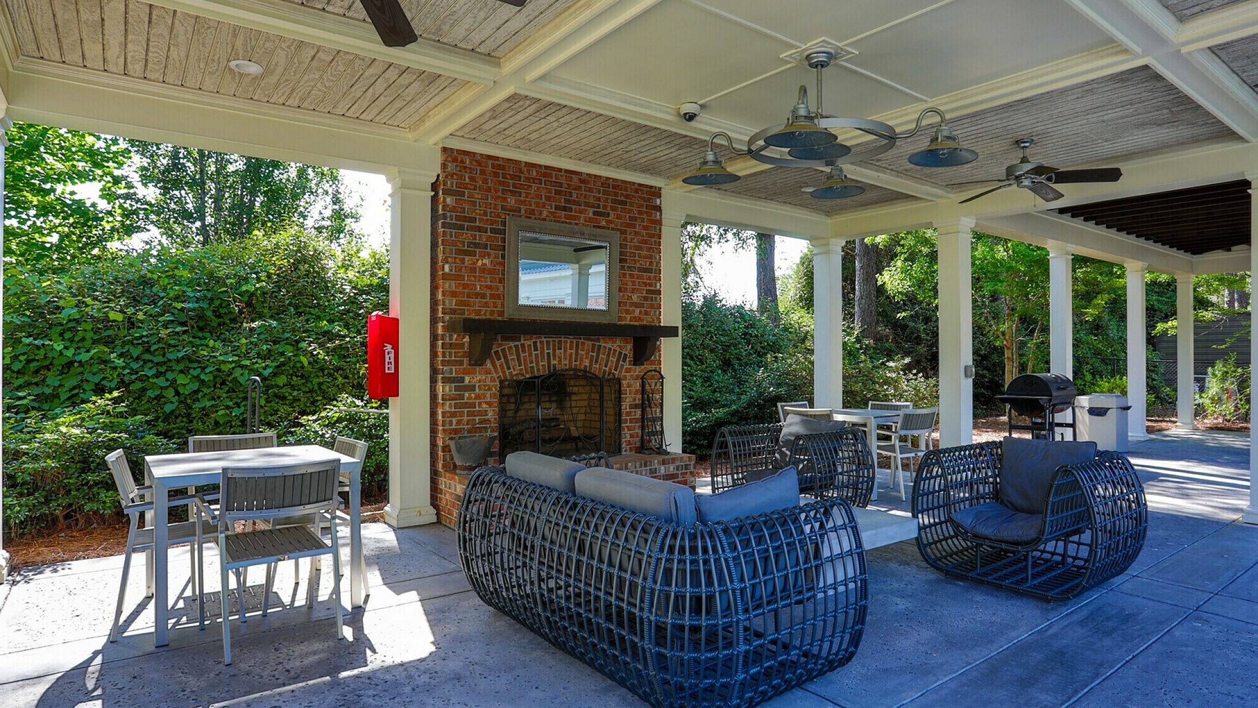 Chic outdoor lounge area featuring cozy wicker furniture, modern ceiling fans, and a rustic brick fireplace, perfect for relaxation and entertaining.
