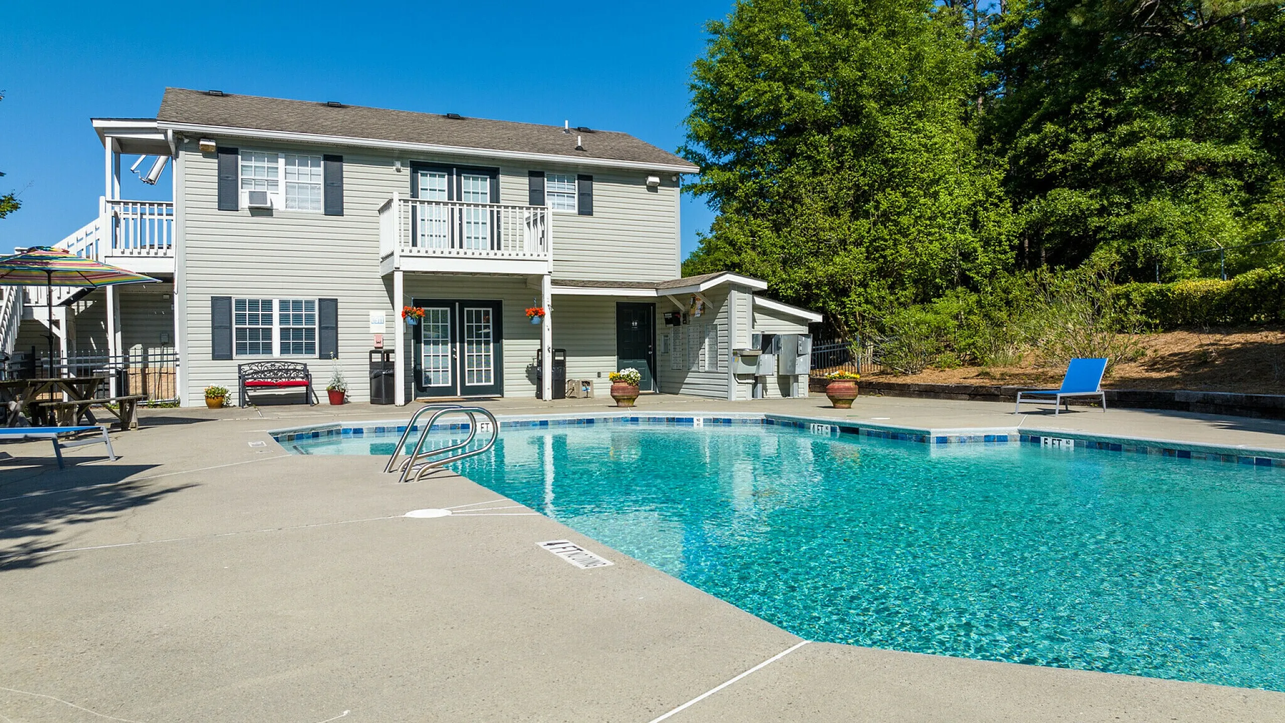 Inviting outdoor pool with crystal-clear water beside a charming two-story house, ideal for relaxation under the bright blue sky.