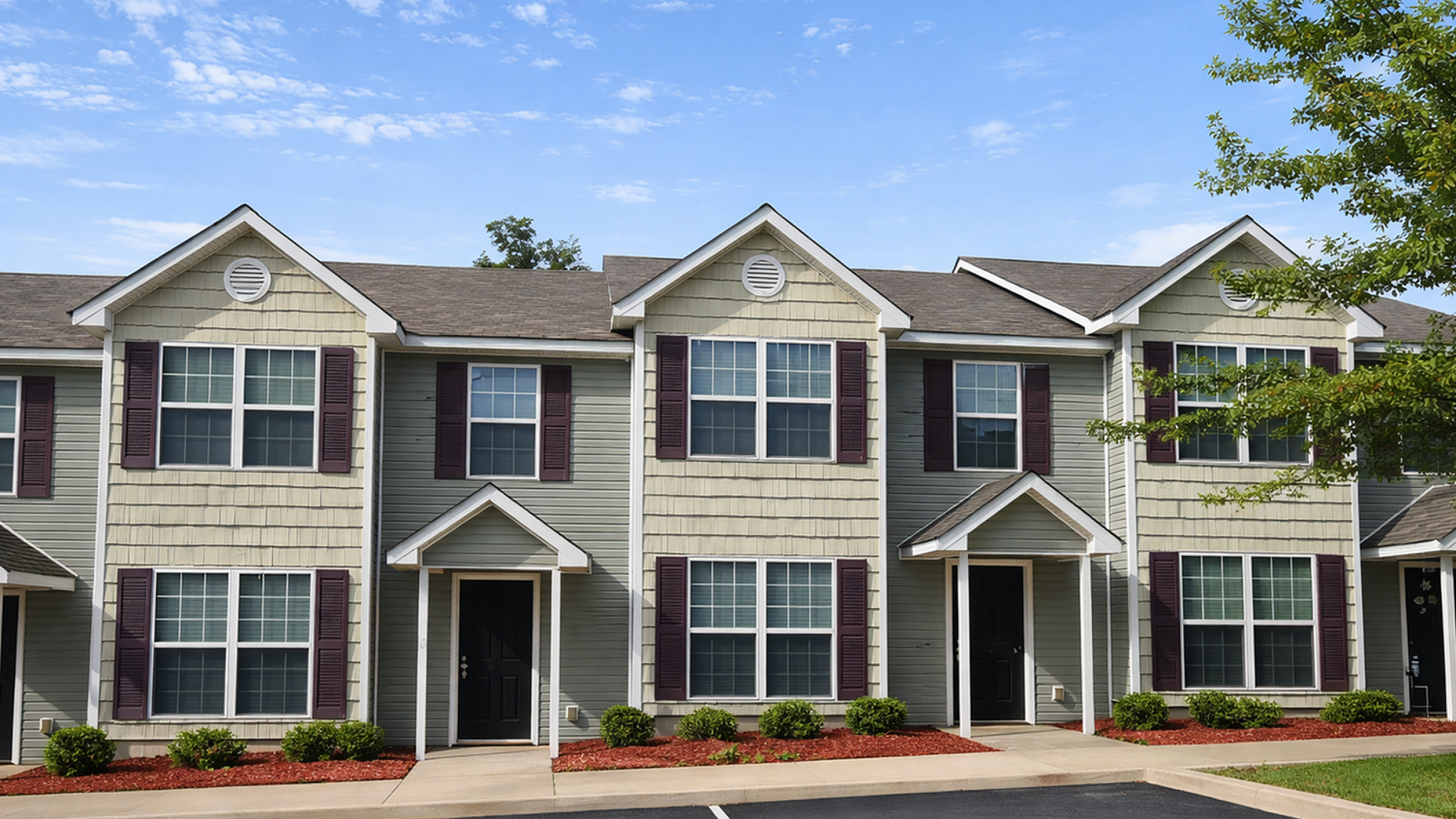 Charming townhouse facade with elegant windows, well-maintained landscaping, and inviting entryway under a clear blue sky.
