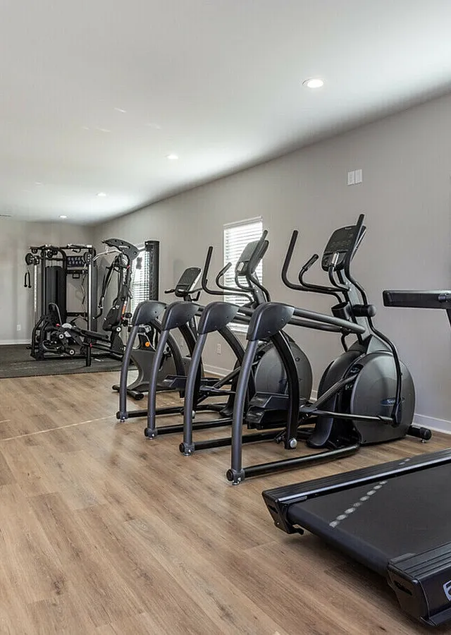 Modern fitness center featuring state-of-the-art treadmills, elliptical machines, and strength training equipment on elegant wooden flooring.