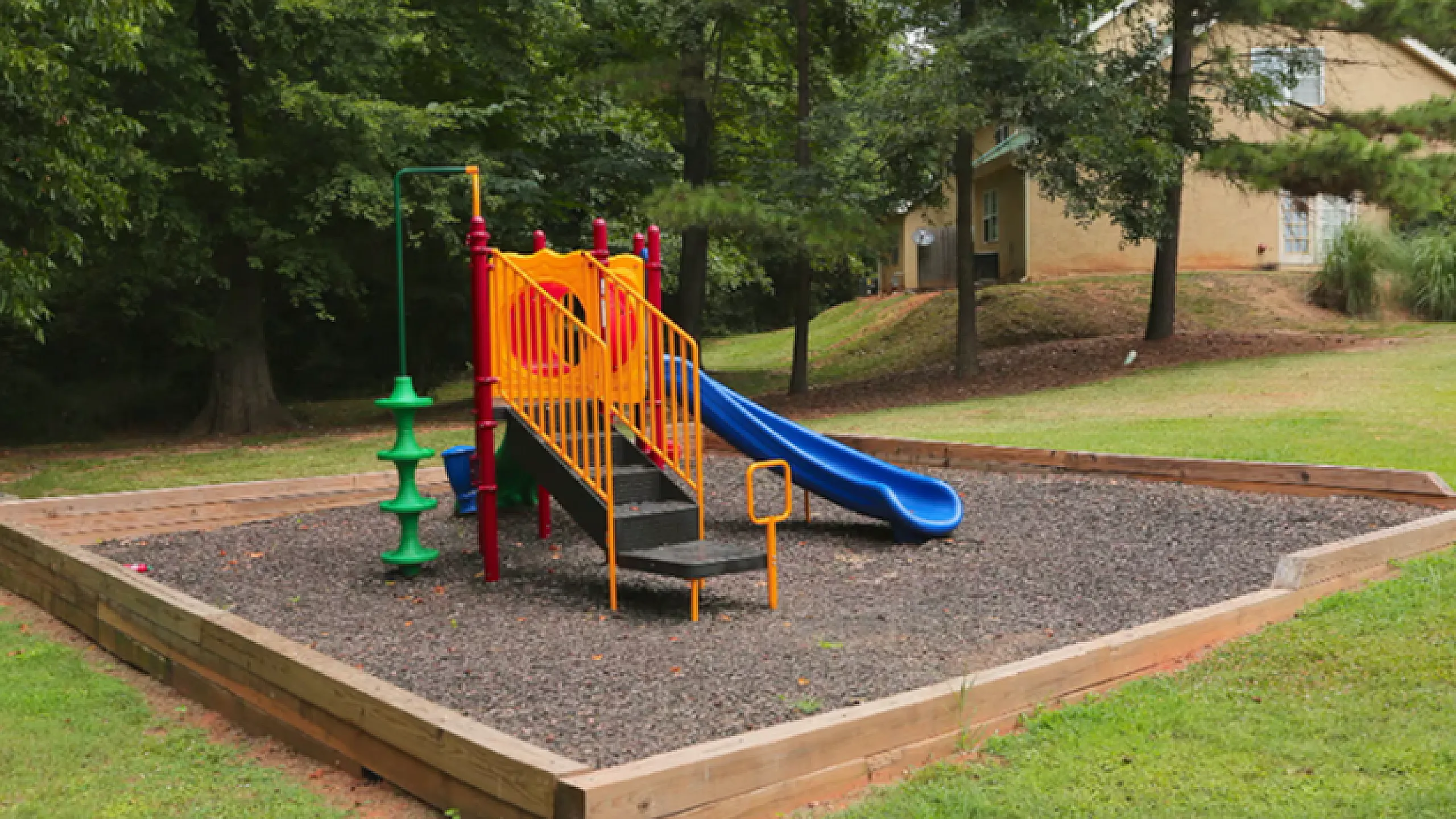 Charming playground featuring a vibrant slide and climbing structures, nestled amid lush greenery, perfect for family fun.