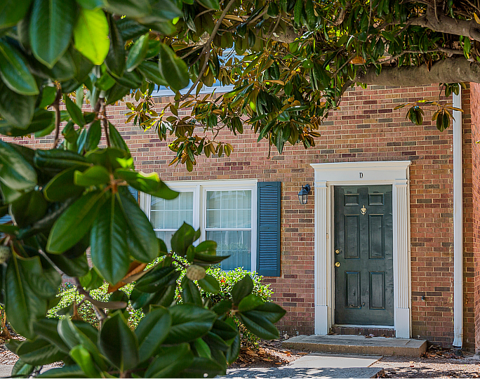 Charming brick apartment with a welcoming entrance framed by lush green foliage, offering a cozy and serene living space.