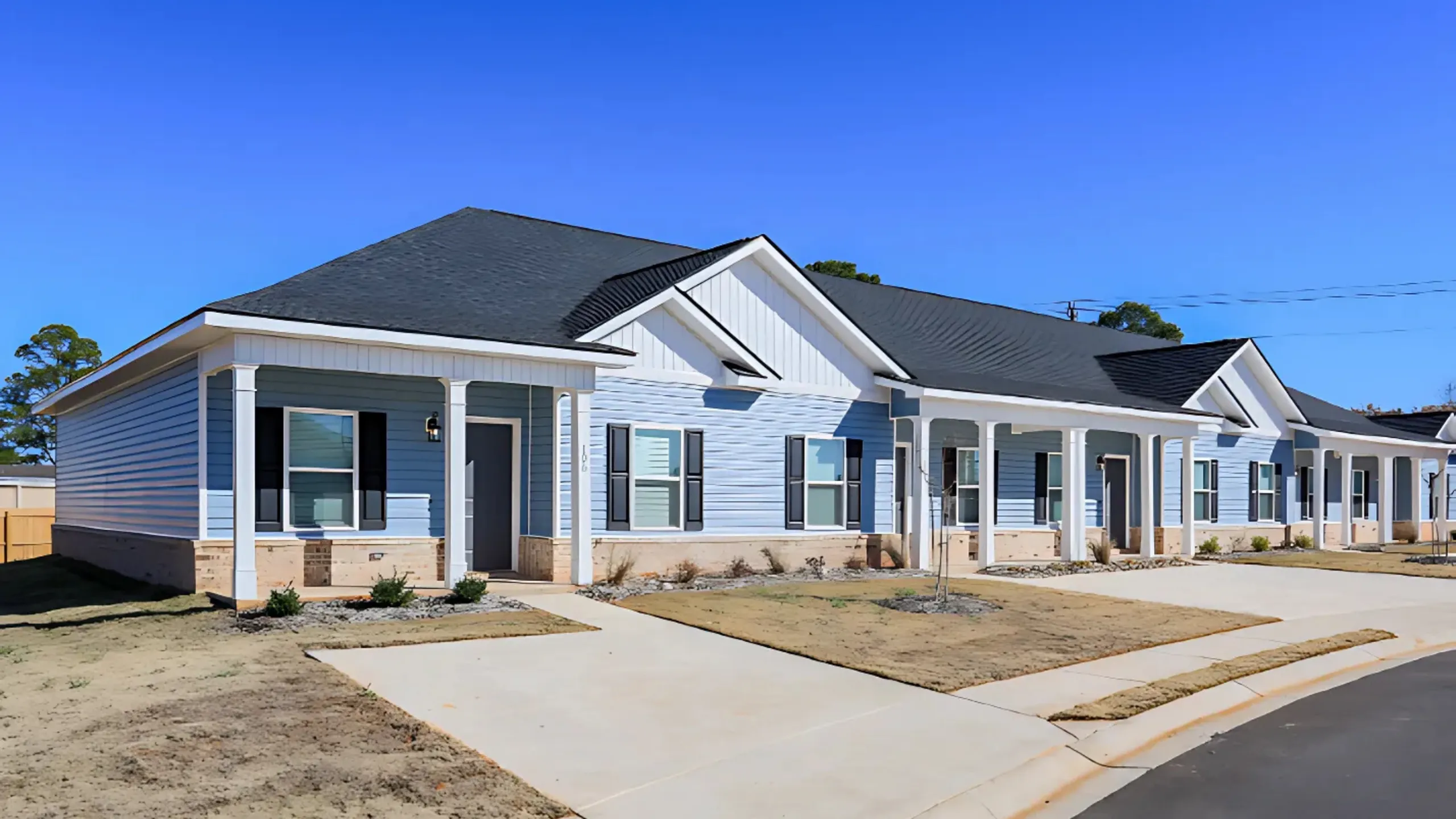 Charming row of modern townhouses with blue siding, white trim, and welcoming front porches in a sunny neighborhood.