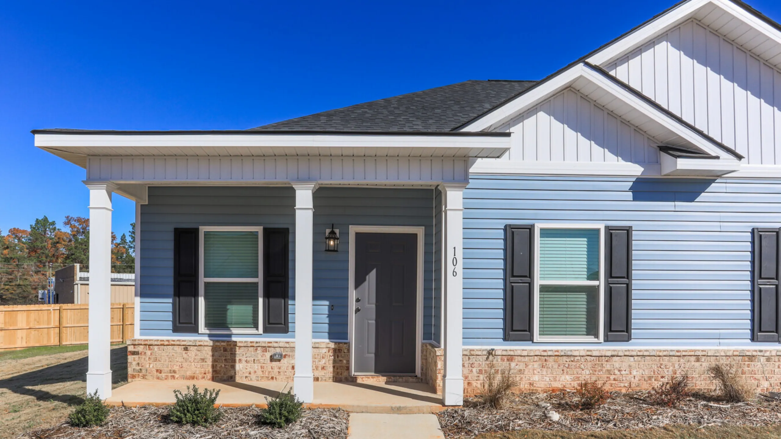 Charming modern home exterior featuring blue siding, sleek black shutters, and elegant white columns under a clear blue sky.