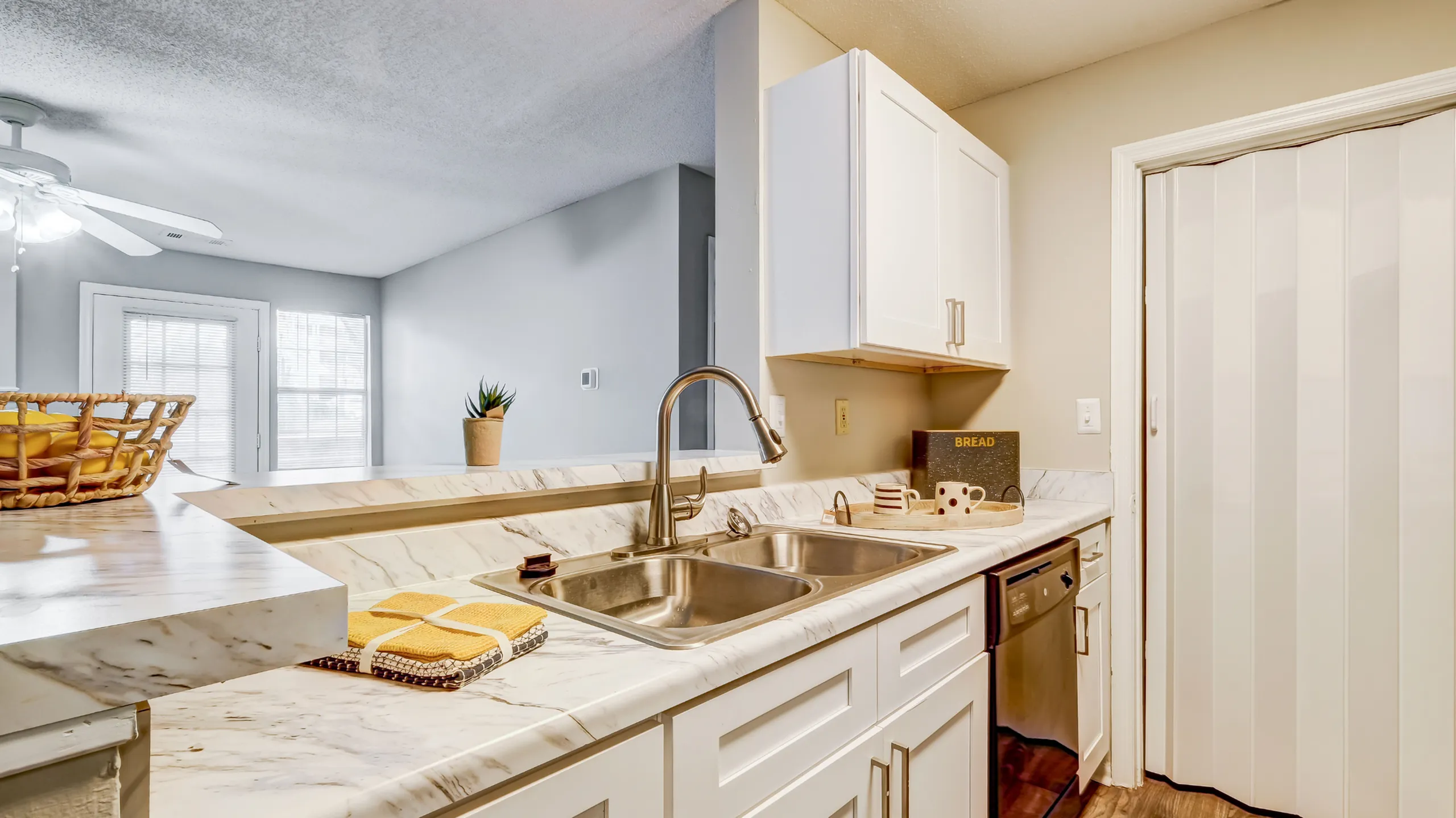 Elegant kitchen with sleek marble countertops, stainless steel sink, and stylish white cabinetry, offering a bright and inviting atmosphere.