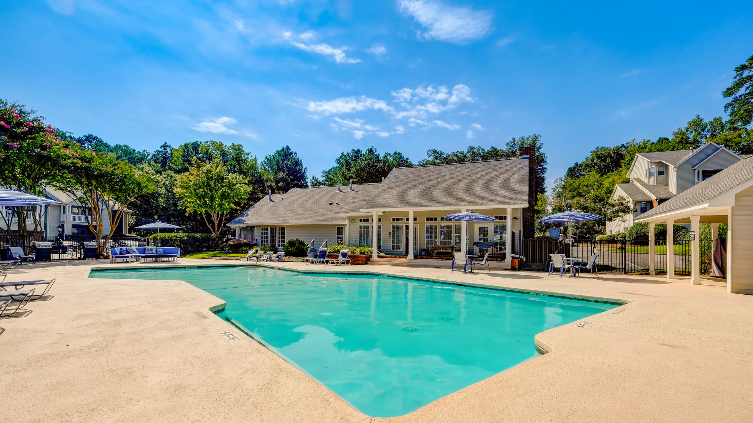 Inviting luxury apartment complex featuring a sparkling pool, surrounded by comfortable lounge spaces and vibrant greenery.