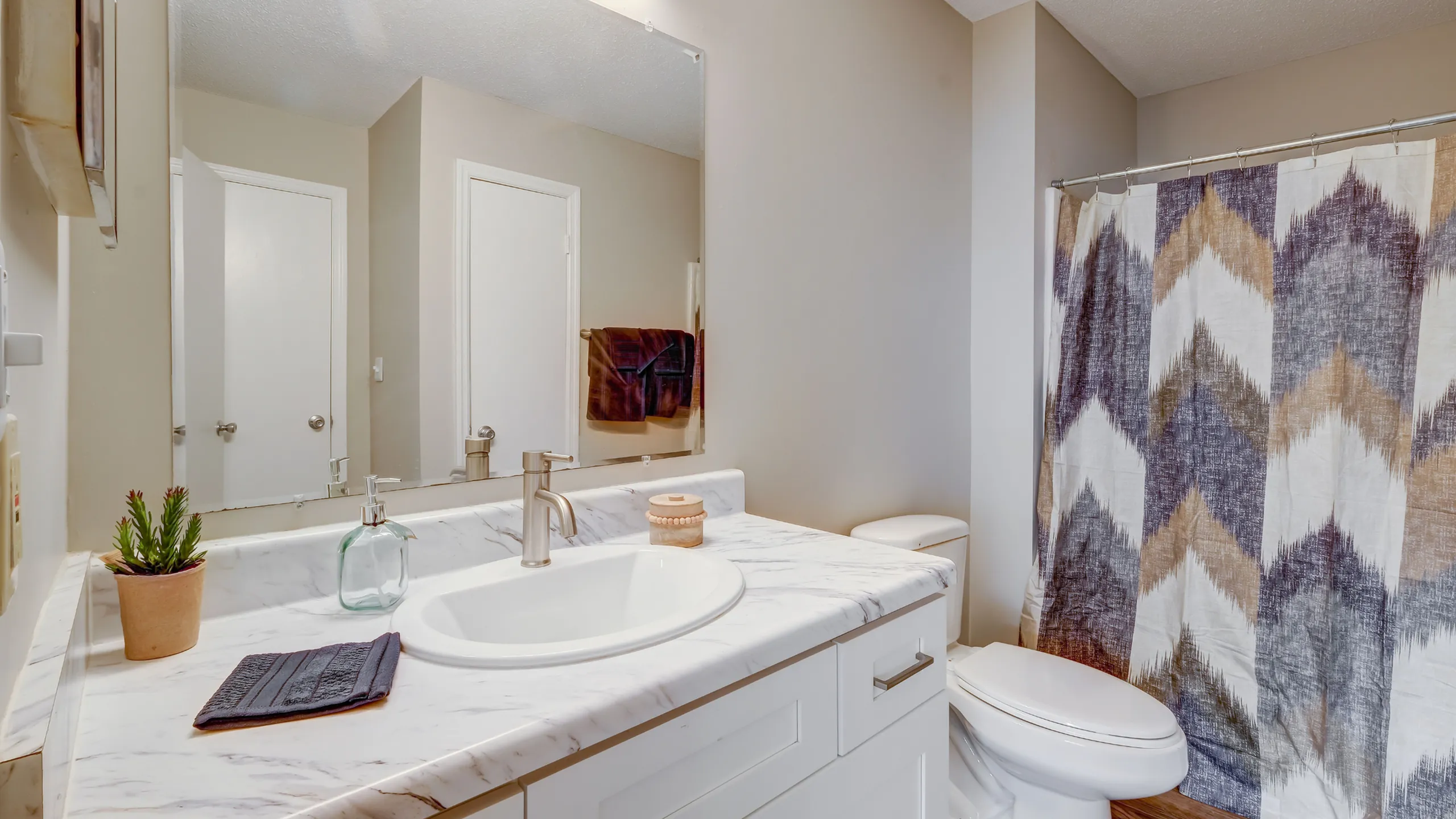 Bright and modern bathroom with elegant marble countertops, stylish faucet, and chic chevron shower curtain.