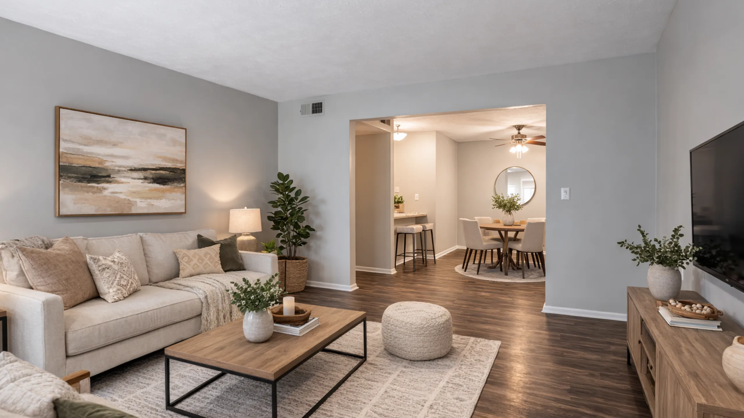 Charming open living area with elegant decor, cozy beige sofa, modern artwork, and a connected dining space featuring soft lighting and wooden floors.
