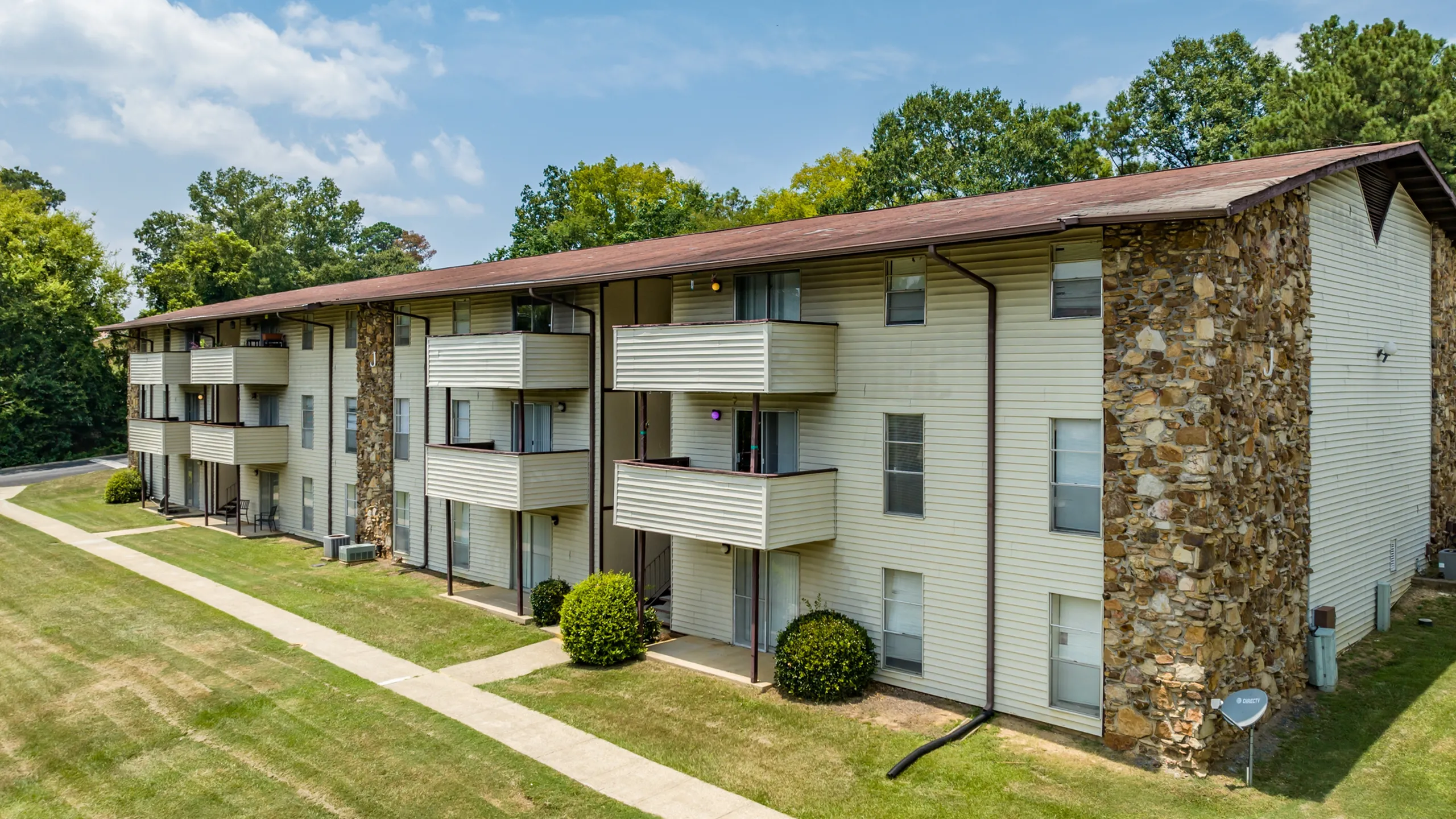 Charming three-story apartment building featuring spacious balconies, surrounded by lush greenery and a well-maintained lawn.