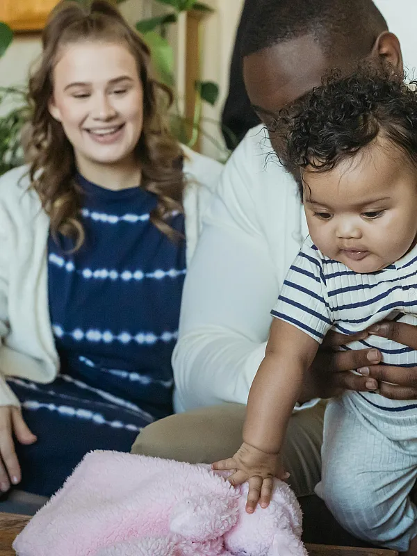 Cozy family living area with natural light, featuring happy parents and a baby enjoying their stylish, plant-accented home.