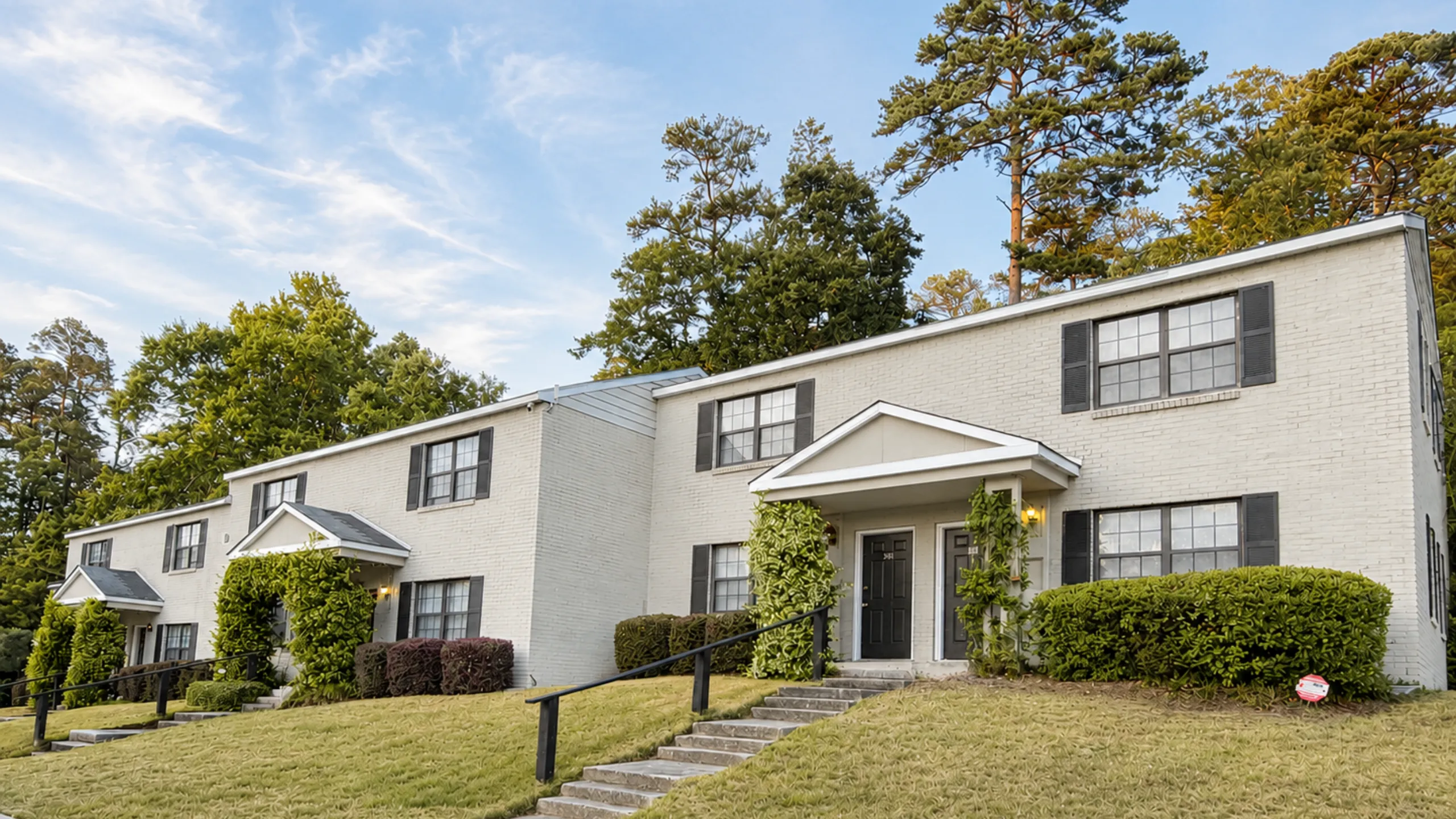 Charming duplex with classic brick exterior, surrounded by lush greenery and a serene environment.