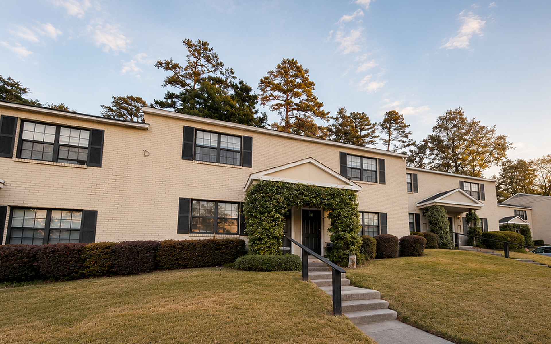 Charming townhouse complex with well-maintained lawns, classic brick exteriors, and lush greenery, perfect for serene living.