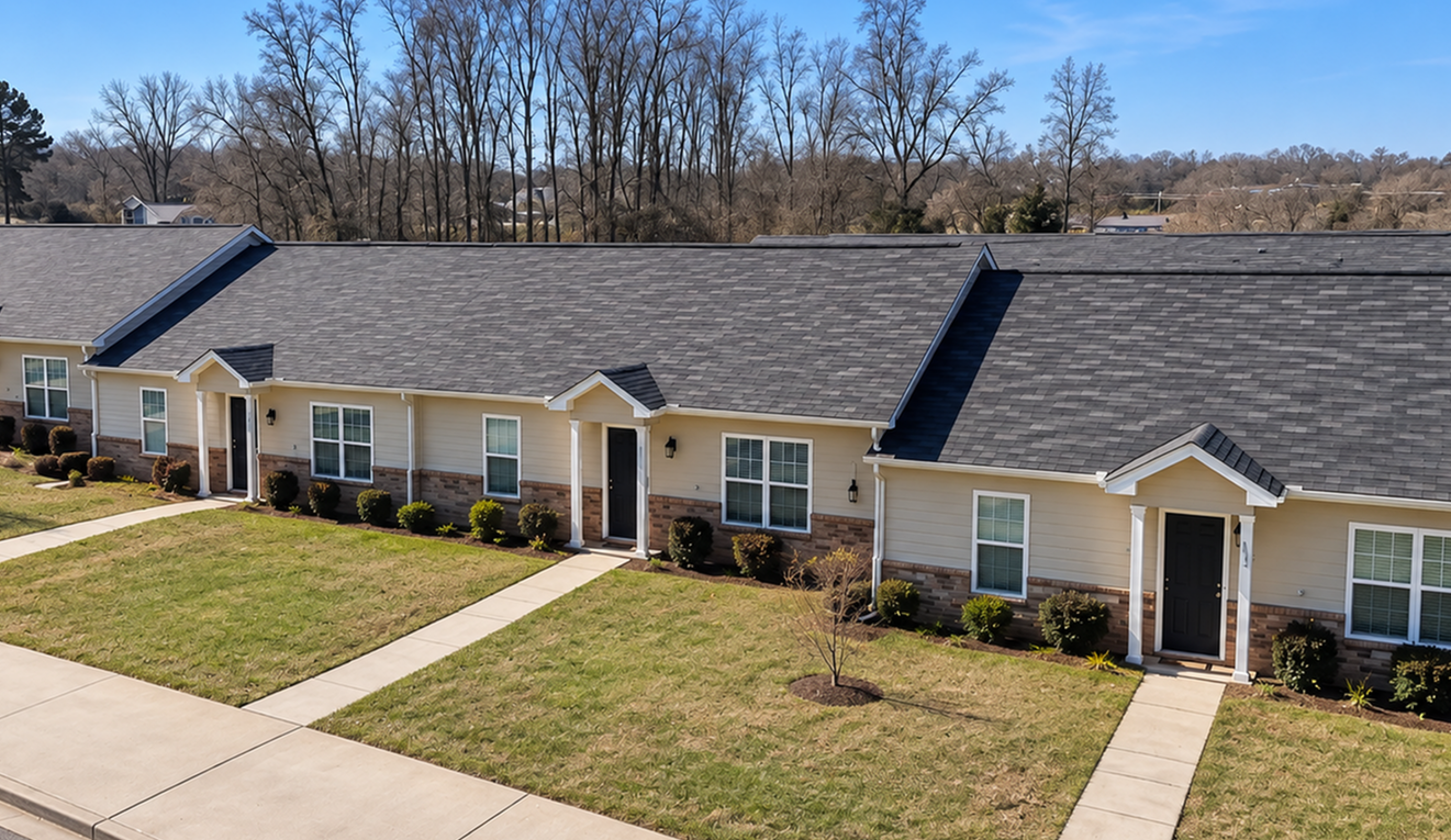 Charming single-story townhouses with manicured lawns and inviting entryways, set against a peaceful suburban backdrop.
