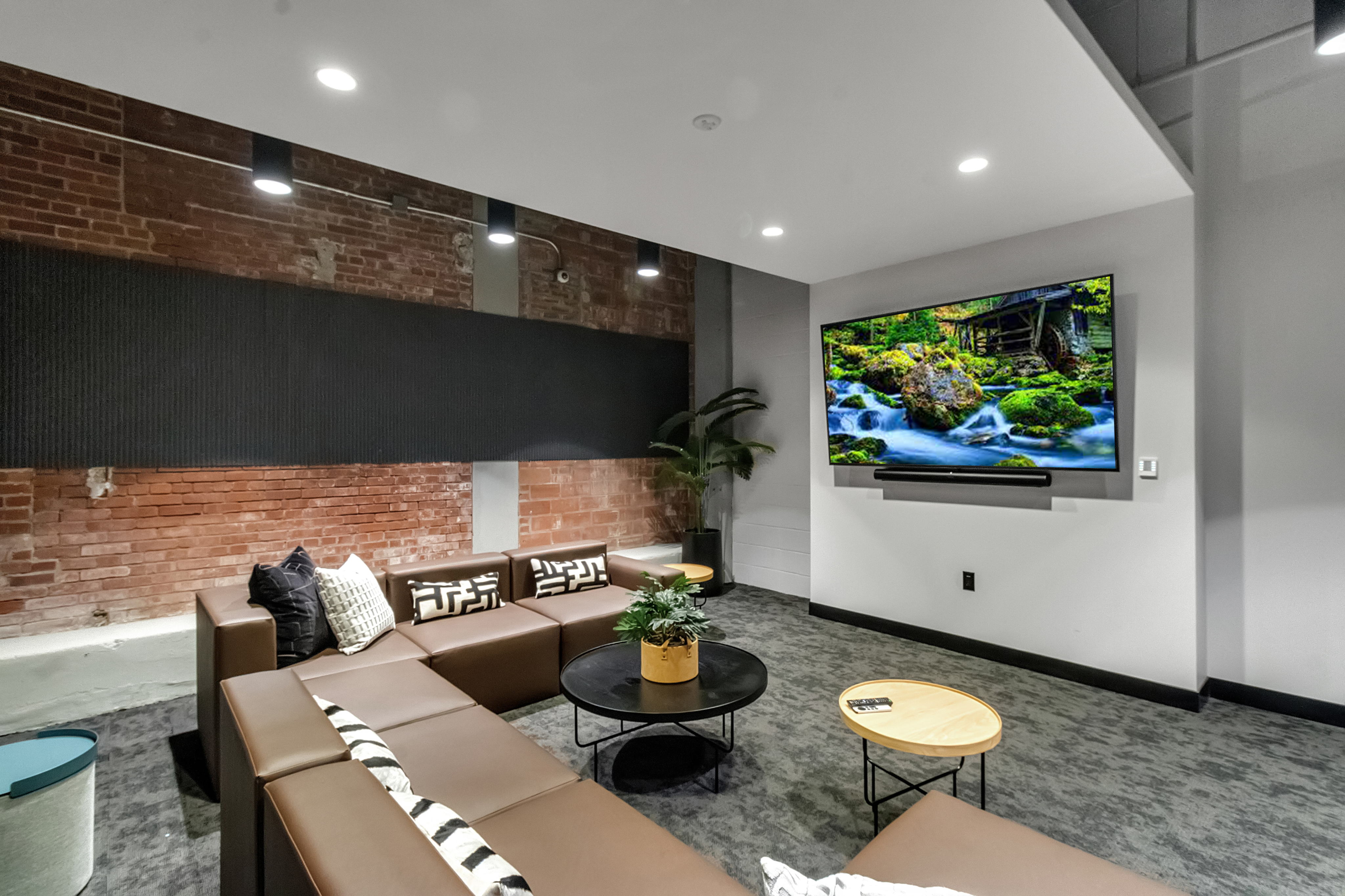 Chic living room with exposed brick, modern brown sectional sofa, and large flat-screen TV, perfect for entertainment and relaxation.