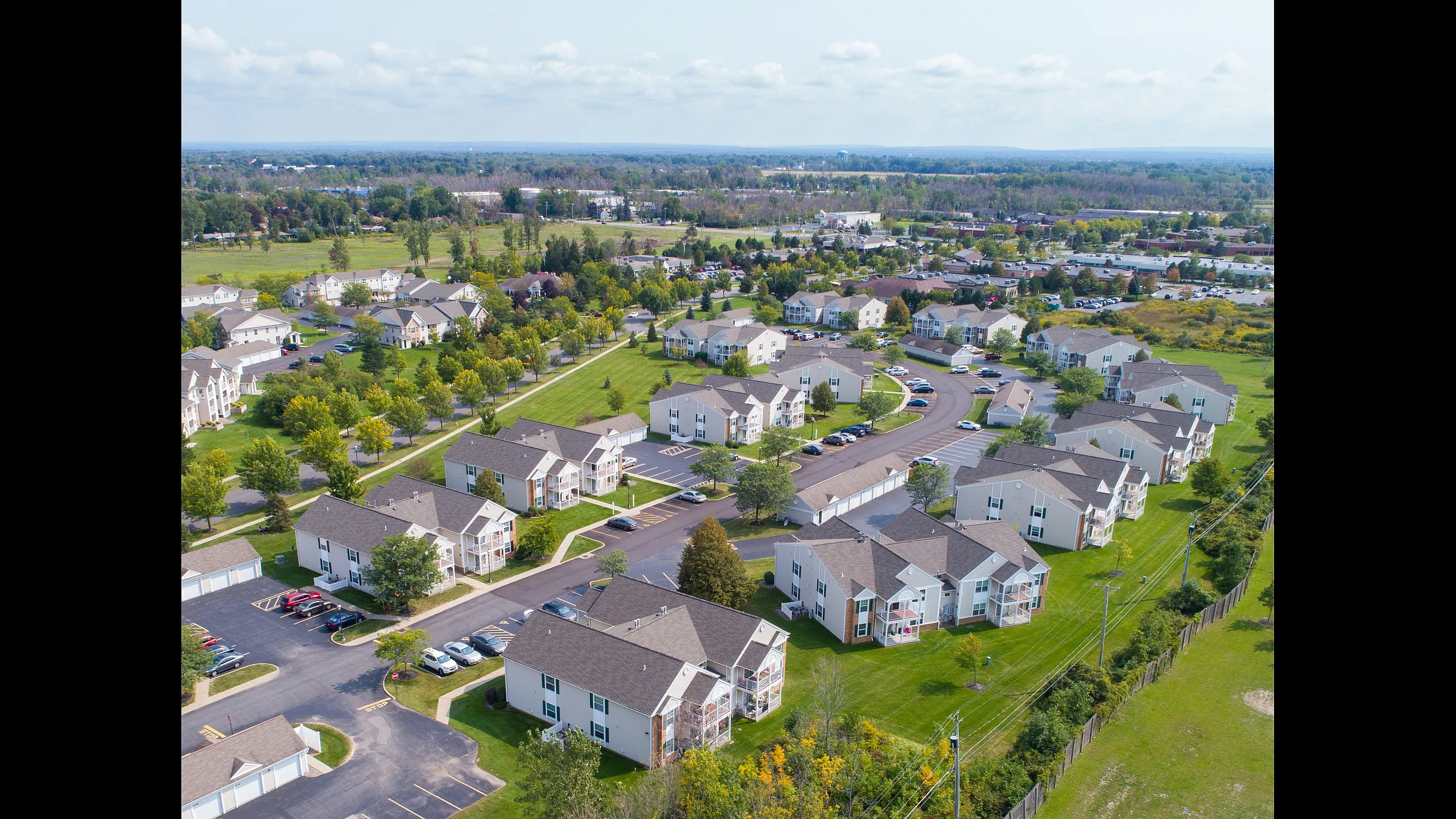 Charming aerial view of a suburban apartment complex surrounded by lush greenery and spacious roads, offering a serene living environment.