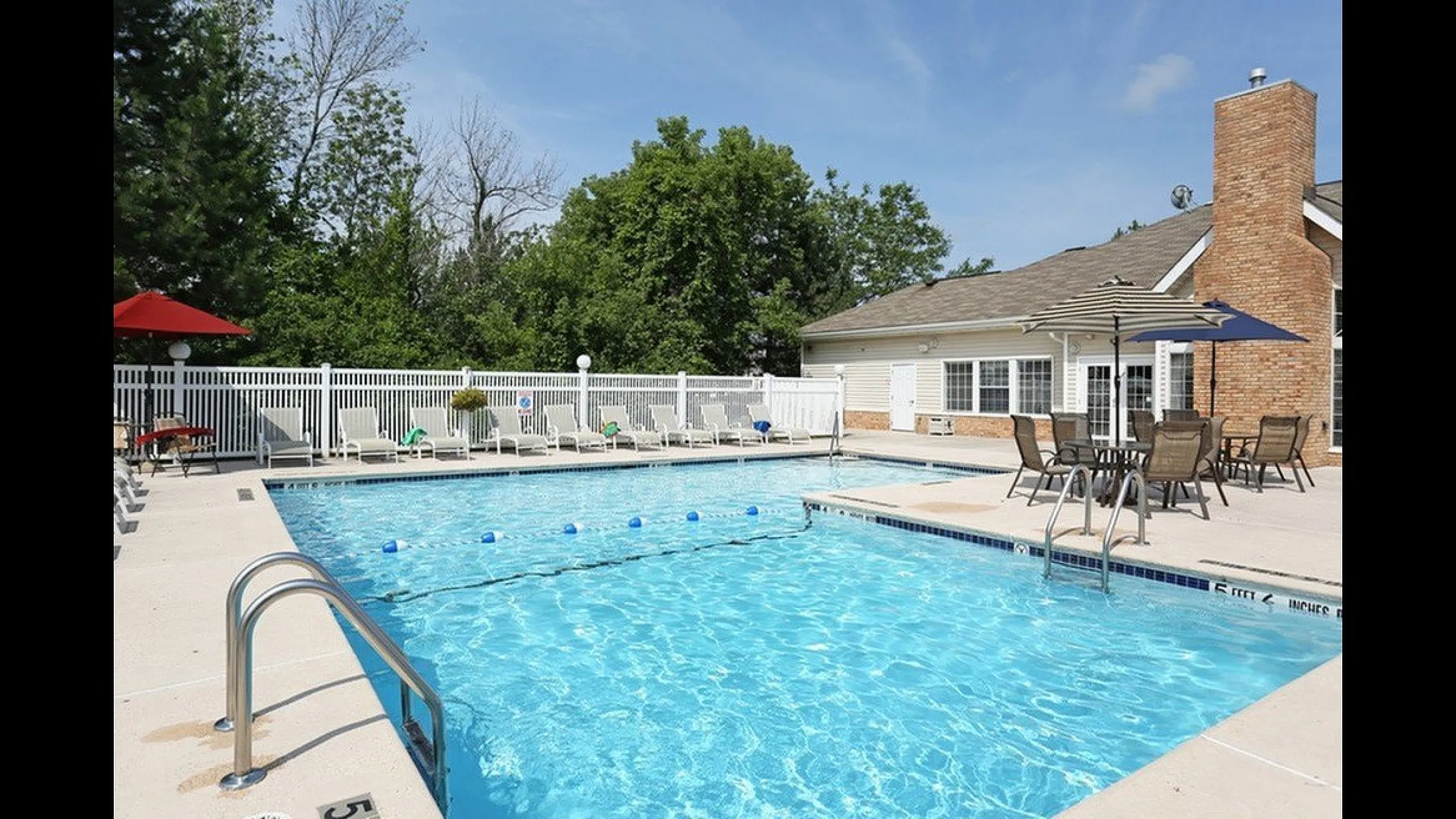 Inviting swimming pool area with sun loungers and patio seating, surrounded by lush greenery and a stylish clubhouse.