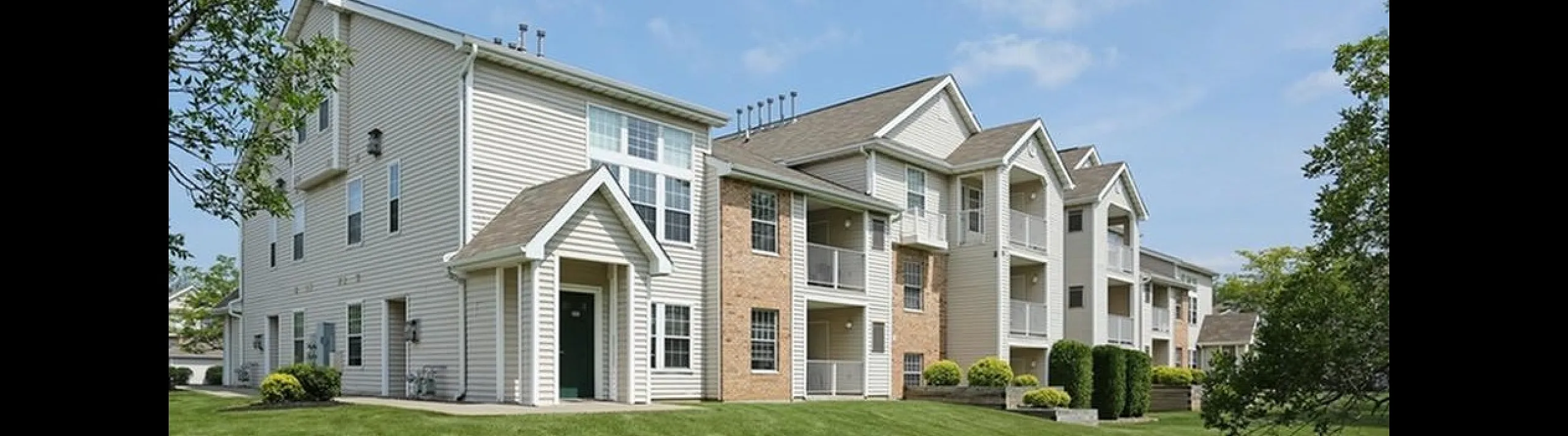 Charming multi-level apartment complex with balconies, surrounded by lush green lawns and scenic trees, perfect for modern living.