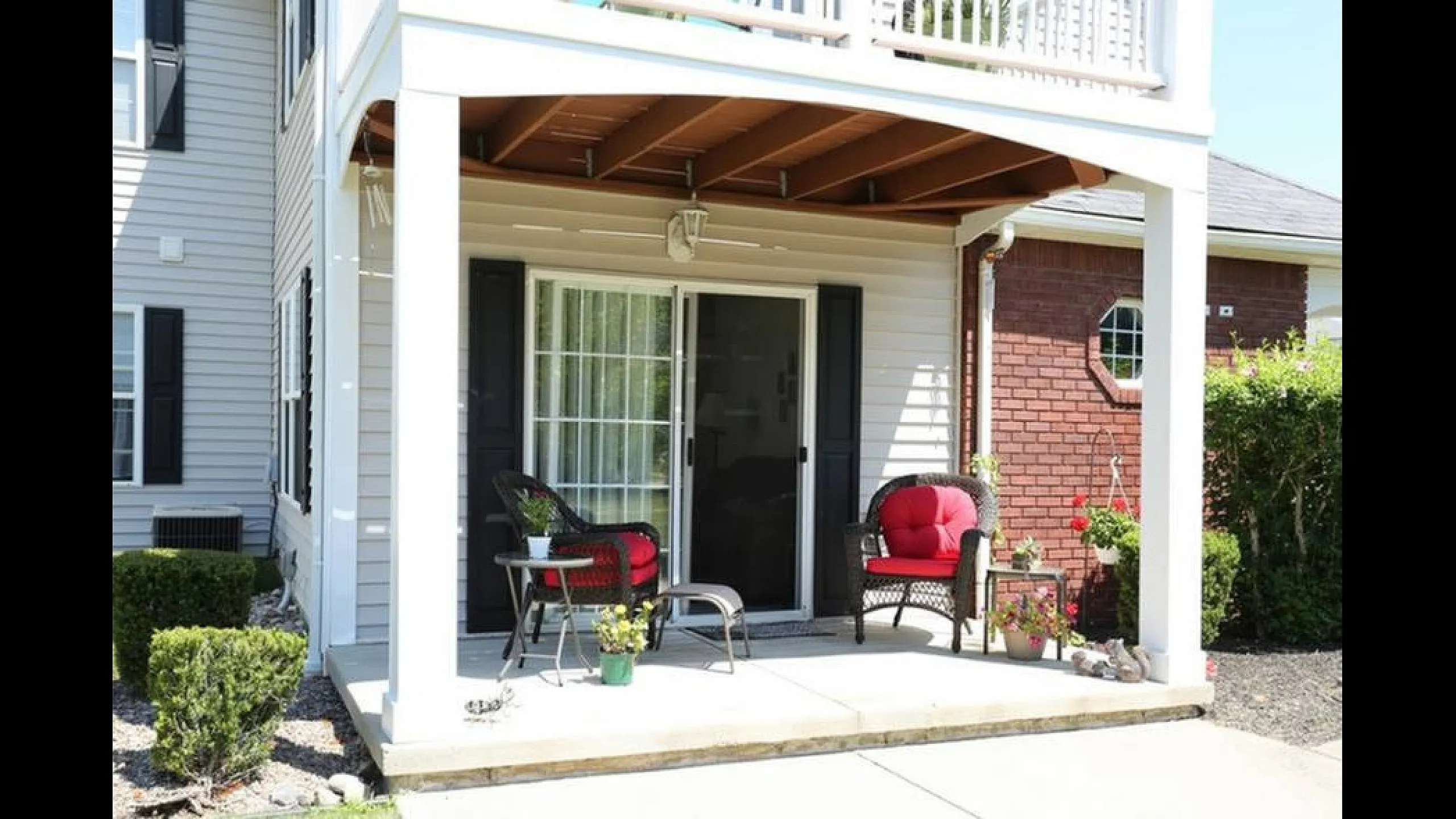 Charming patio space with cozy red-cushioned seating and lush greenery, perfect for relaxing afternoons.