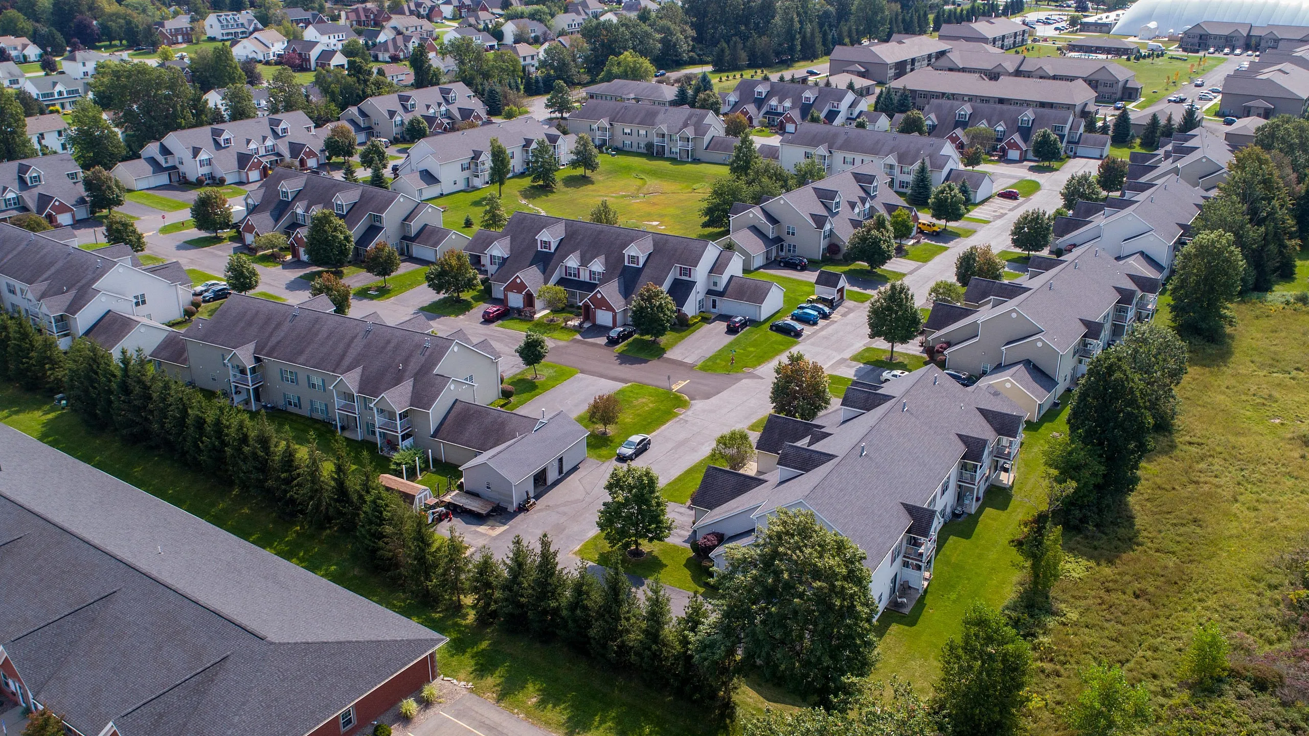 Aerial view of a picturesque suburban apartment community with tree-lined streets, modern homes, and ample green spaces.