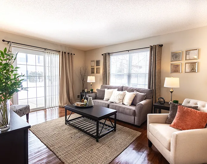 Cozy living room with soft, neutral tones featuring a comfortable gray sofa, elegant accent chairs, and abundant natural light from large windows.