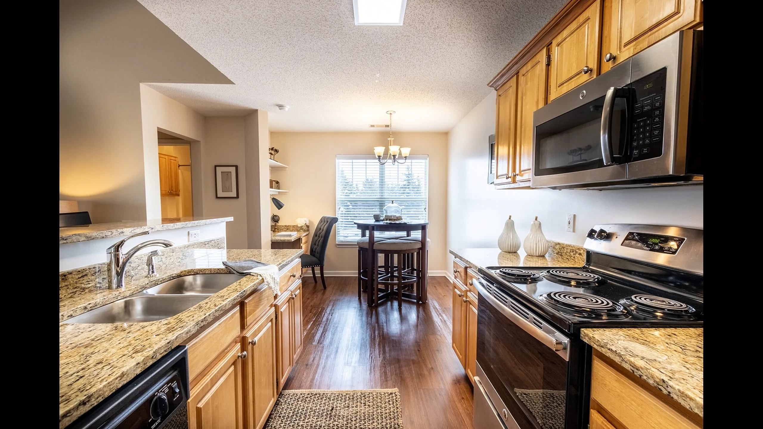 Modern kitchen with warm wood cabinetry, granite countertops, sleek stainless steel appliances, and cozy dining area with natural light.