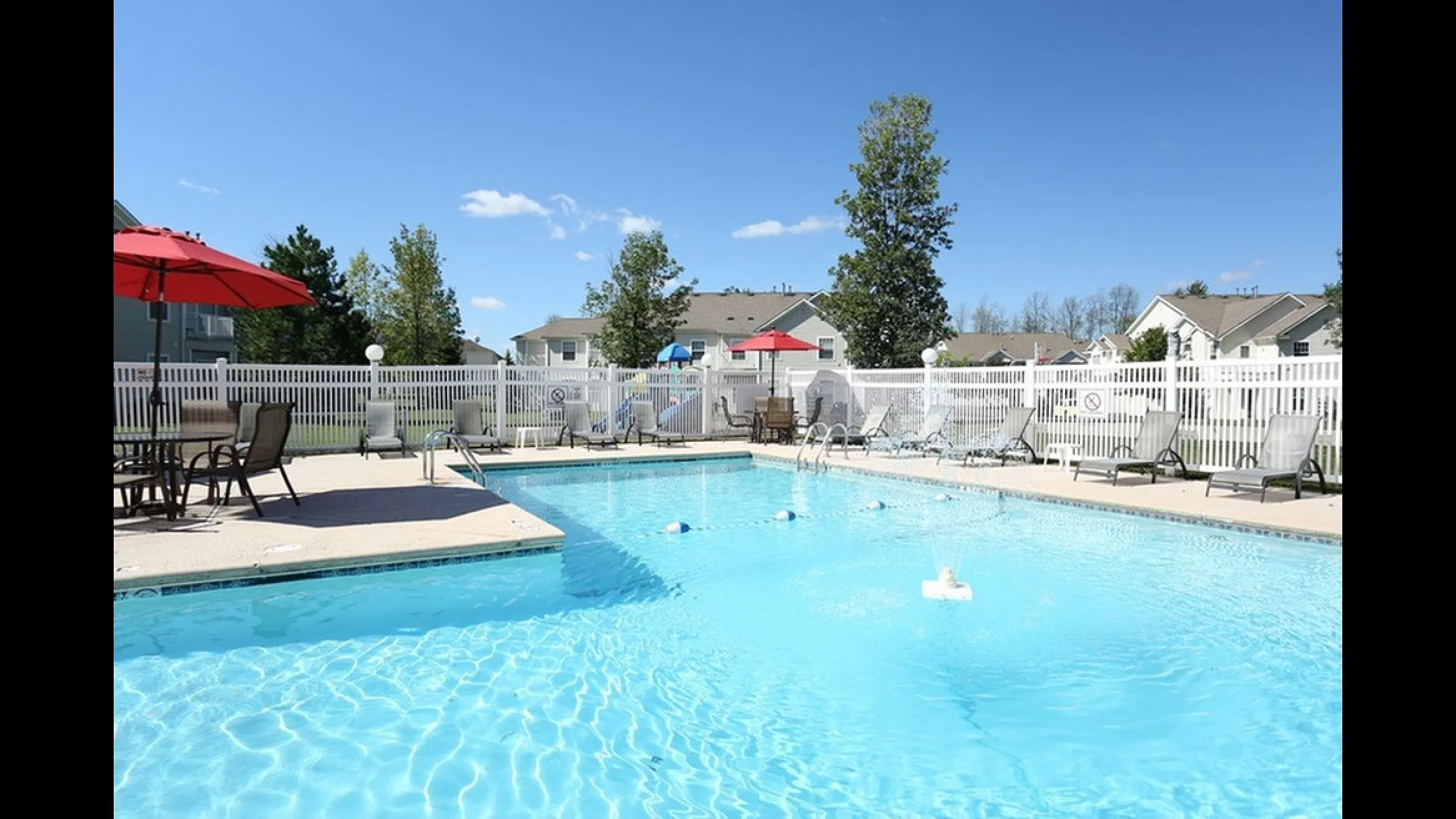 Inviting outdoor pool area with sun loungers and vibrant red umbrellas, perfect for relaxation in a serene residential setting.
