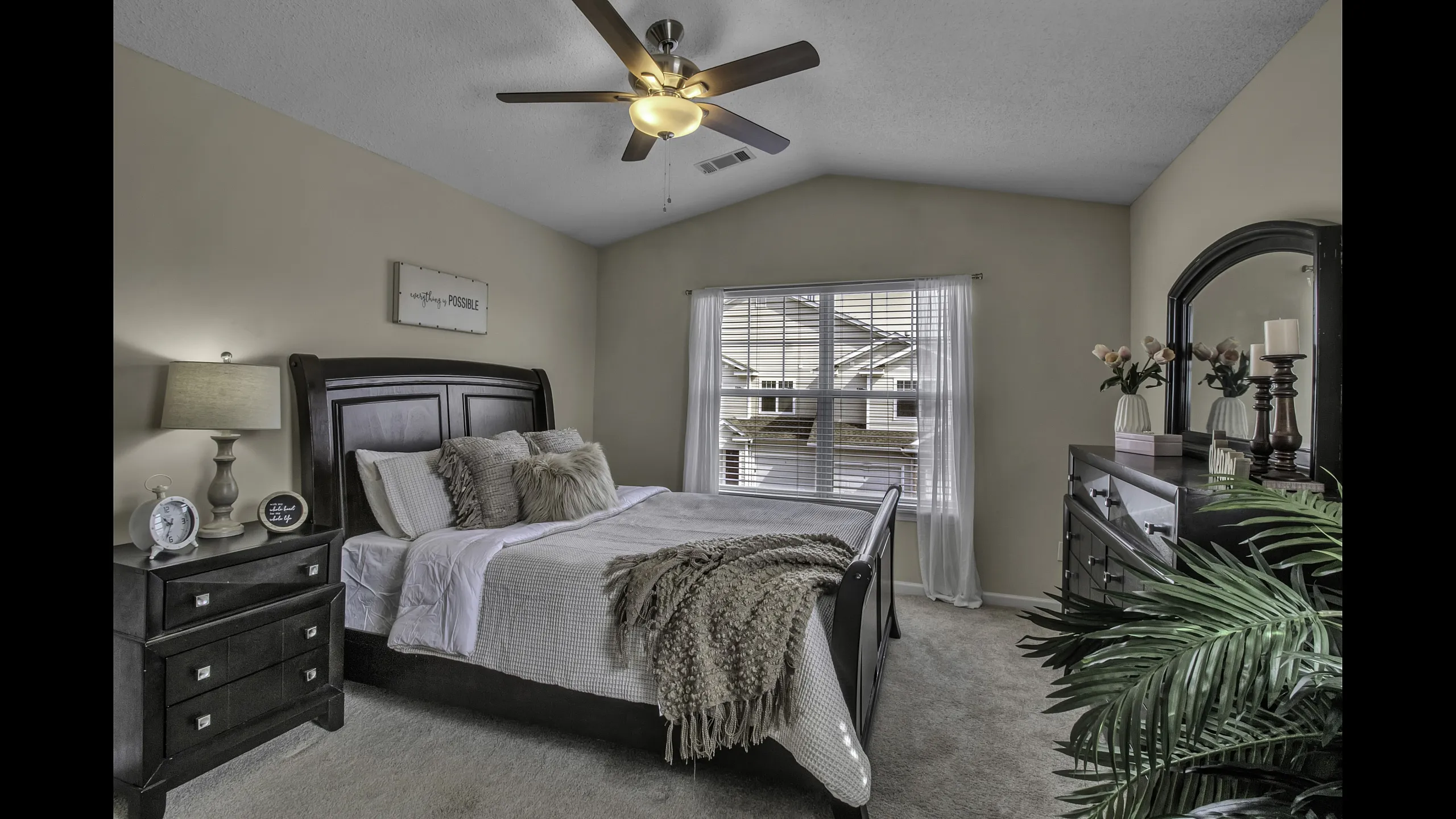 Inviting bedroom with plush bedding, a stylish dark wood dresser, and abundant natural light from large window.