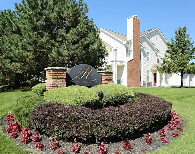 Charming apartment complex with manicured landscaping and elegant sign, offering serene living amidst lush greenery and bright sunny skies.