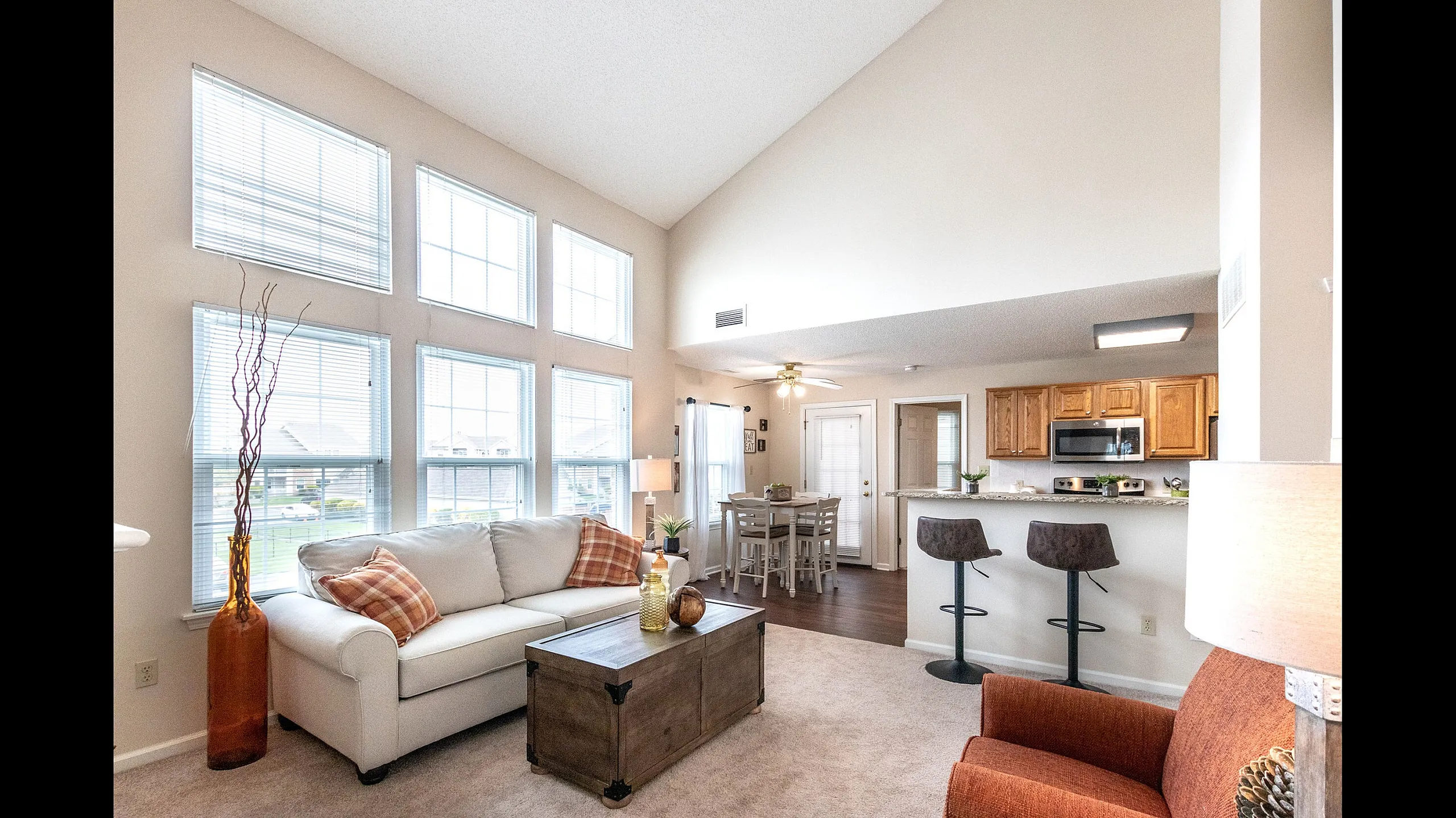 Bright and inviting open-concept living space with high ceilings, large windows, cozy seating area, and a modern kitchen with breakfast bar.