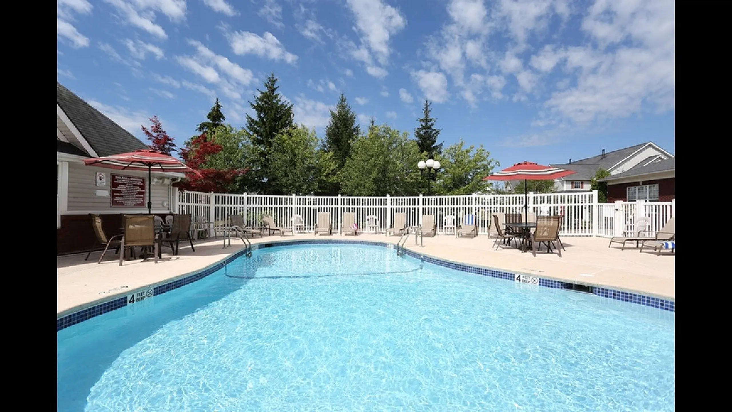 Inviting outdoor pool area with sparkling blue water, surrounded by lounge chairs and red umbrellas, perfect for relaxation and entertainment under a clear sky.