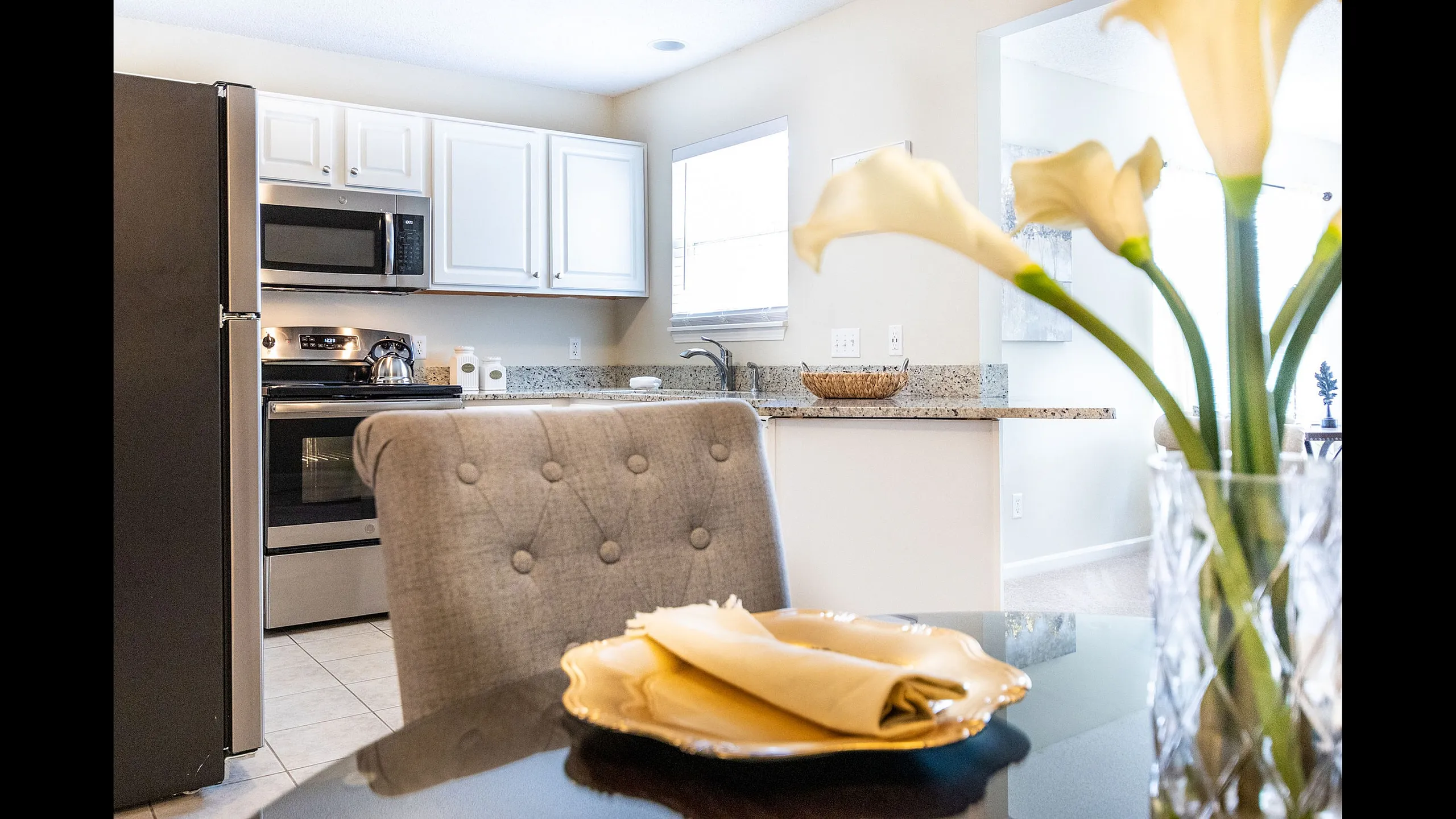 Modern kitchen with granite countertops, stainless steel appliances, and elegant dining area accented by fresh flowers.