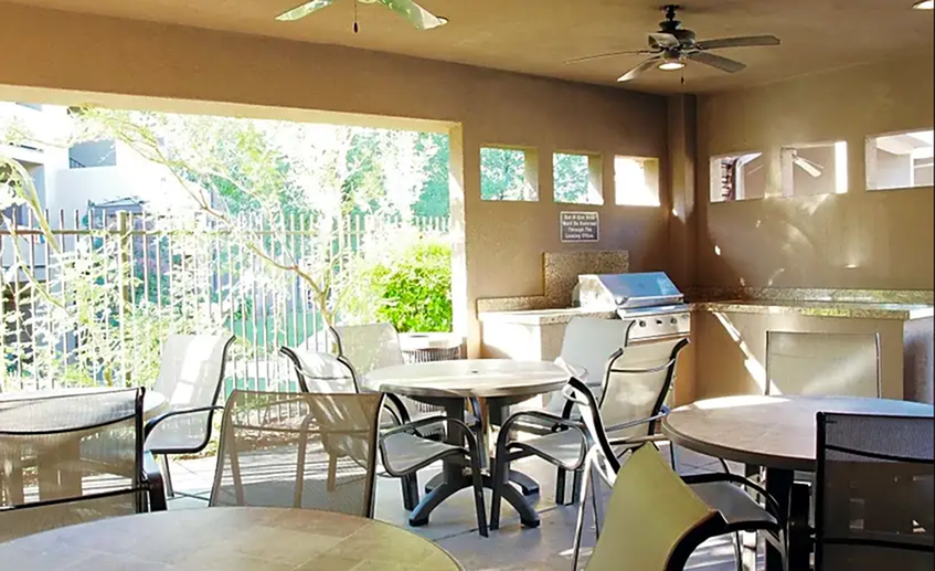 Grill area with 4 round tables with 4 person seating and 1 stainless steel gas grill and granite counter food preparation area