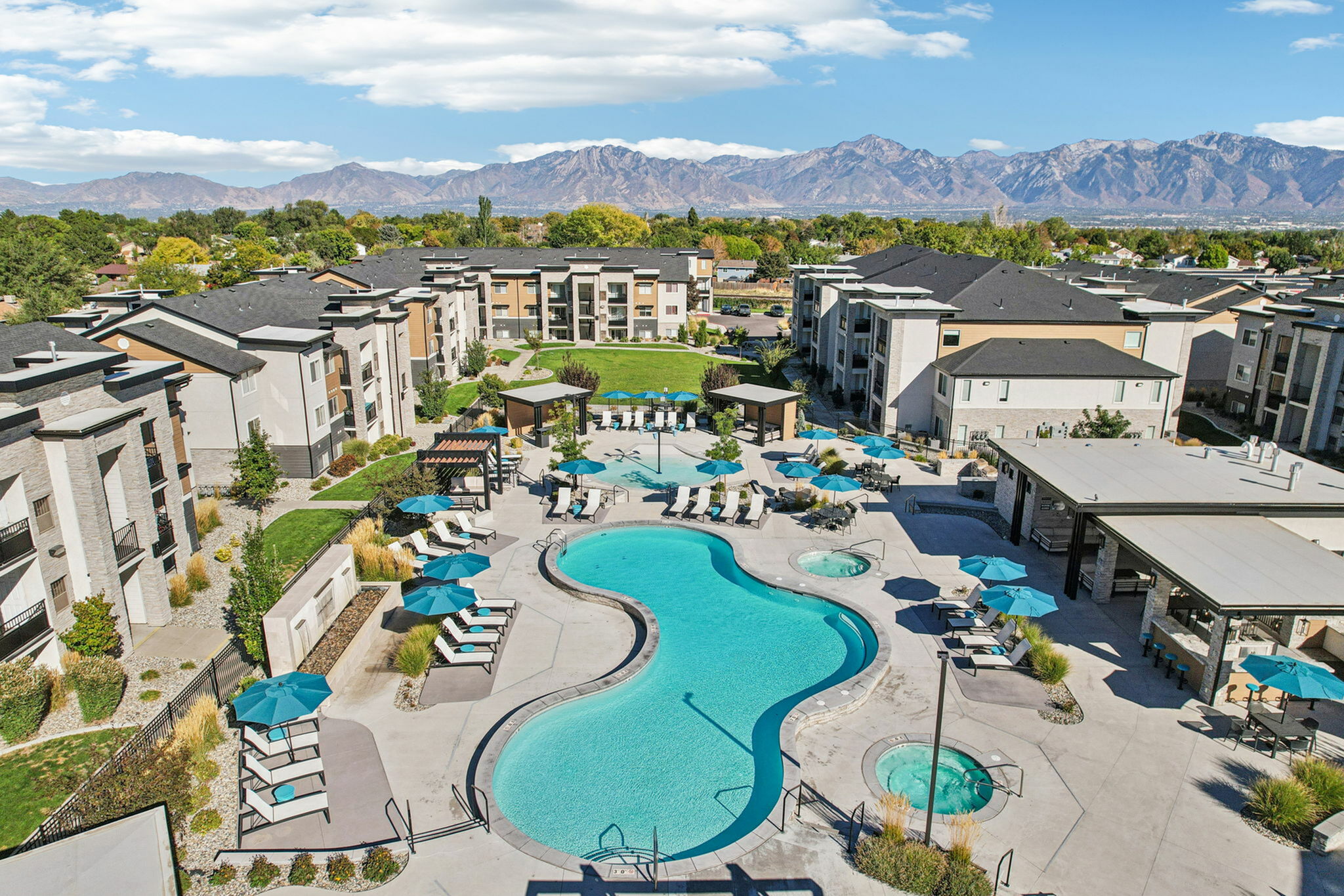 Luxurious apartment complex featuring a stunning swimming pool, lush landscaping, and majestic mountain views.