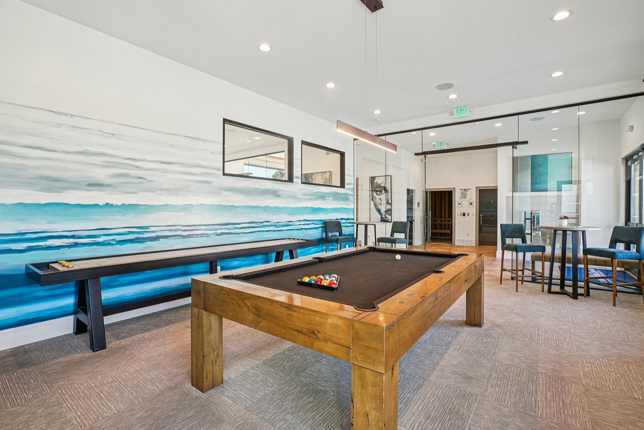 Upscale recreational room featuring a stylish billiard table and modern decor with ocean-themed mural.