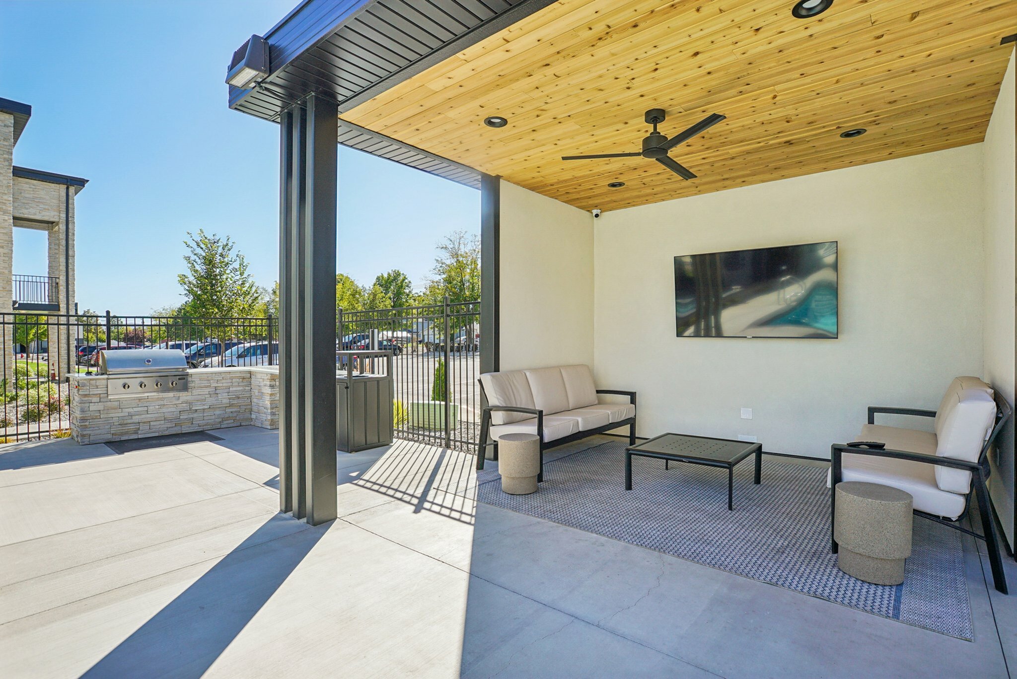 Stylish outdoor lounge area with modern seating, a mounted TV, and a sleek barbecue grill against a backdrop of lush greenery and open sky.