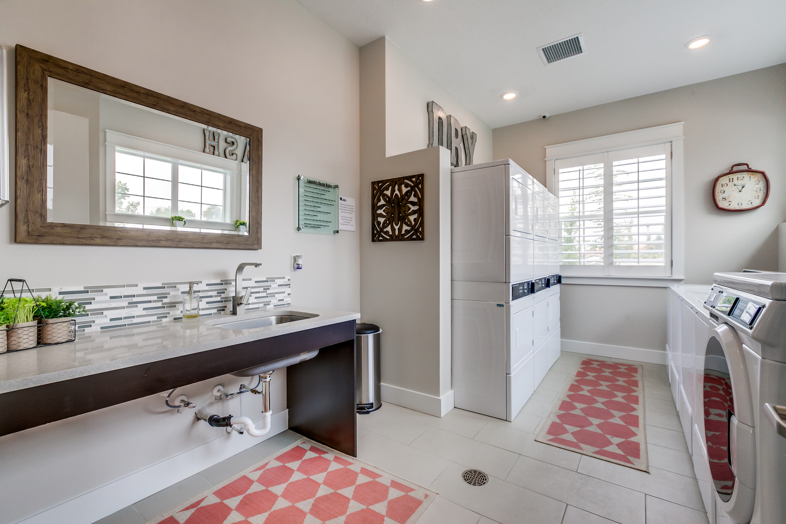 Chic and modern laundry room featuring sleek appliances, a spacious countertop with a stylish backsplash, large mirror, and elegant tile flooring.