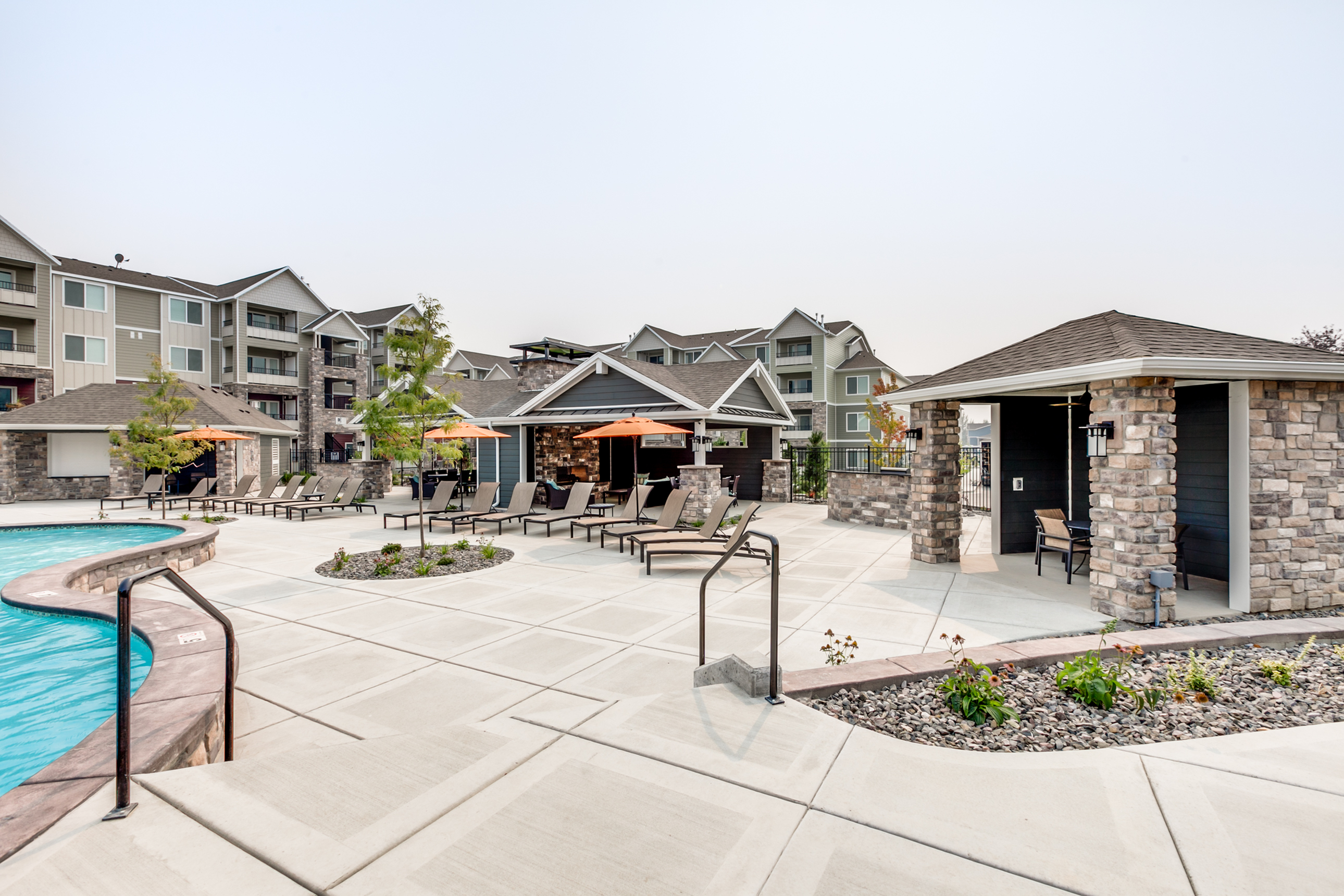 Vibrant apartment complex featuring a luxurious poolside area with stylish loungers and shaded seating, surrounded by modern buildings.