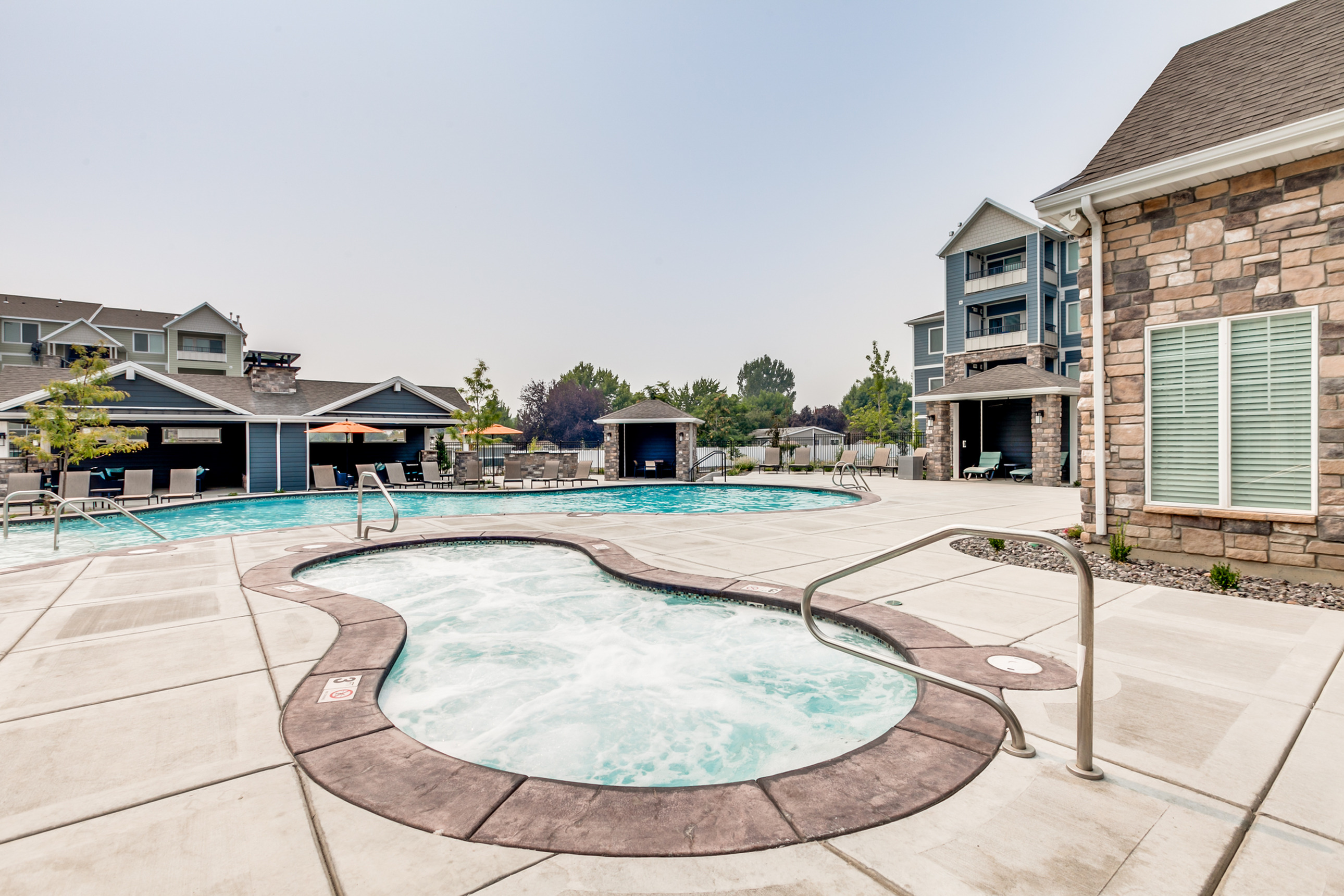 Luxurious apartment complex with a sparkling outdoor pool, elegant hot tub, and modern facilities surrounded by lush greenery.